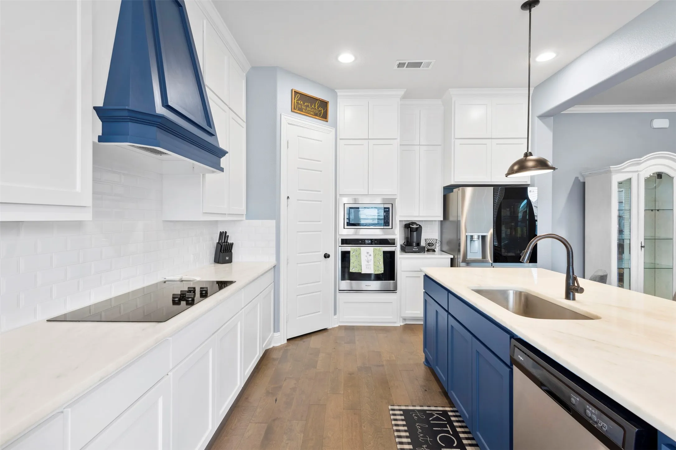 Kitchen featuring a blue custom range hood, white subway tile backsplash, white cabinetry, a kitchen island with a single basin sink, and stainless steel appliances