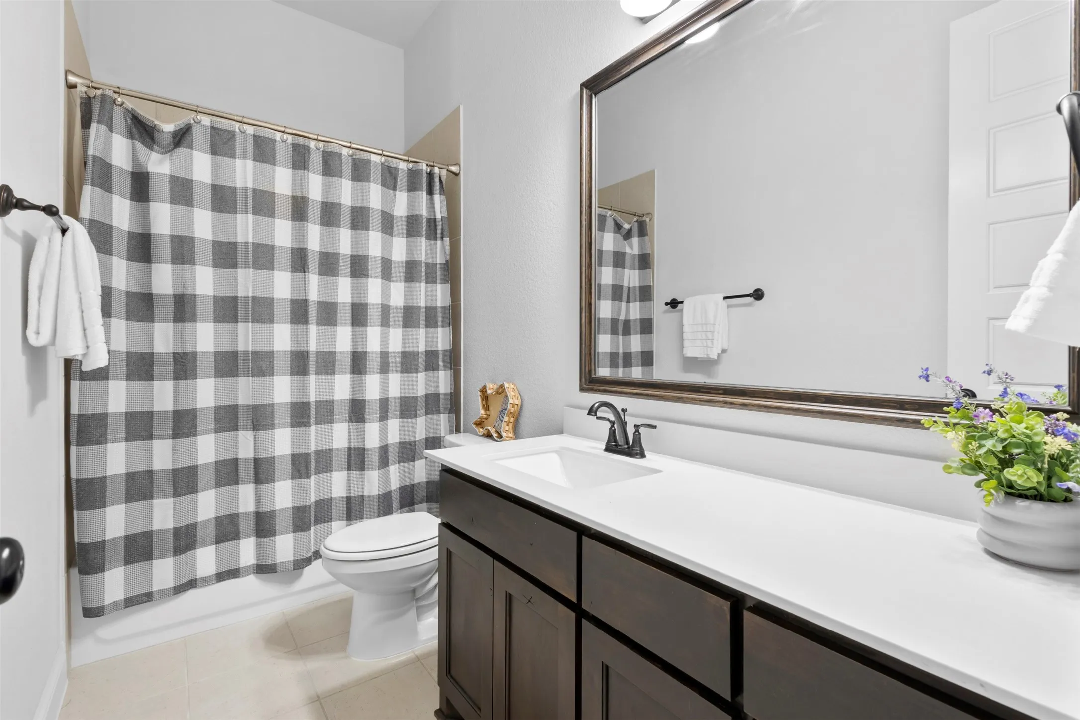 Bathroom featuring a dark wood-finish vanity with ample storage, a white countertop, an integrated rectangular sink, a black-finish faucet, and a large framed mirror