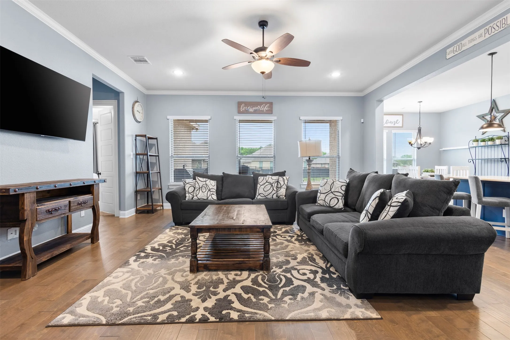 Spacious living area featuring wood-finish flooring, light blue wall tones, and white crown molding