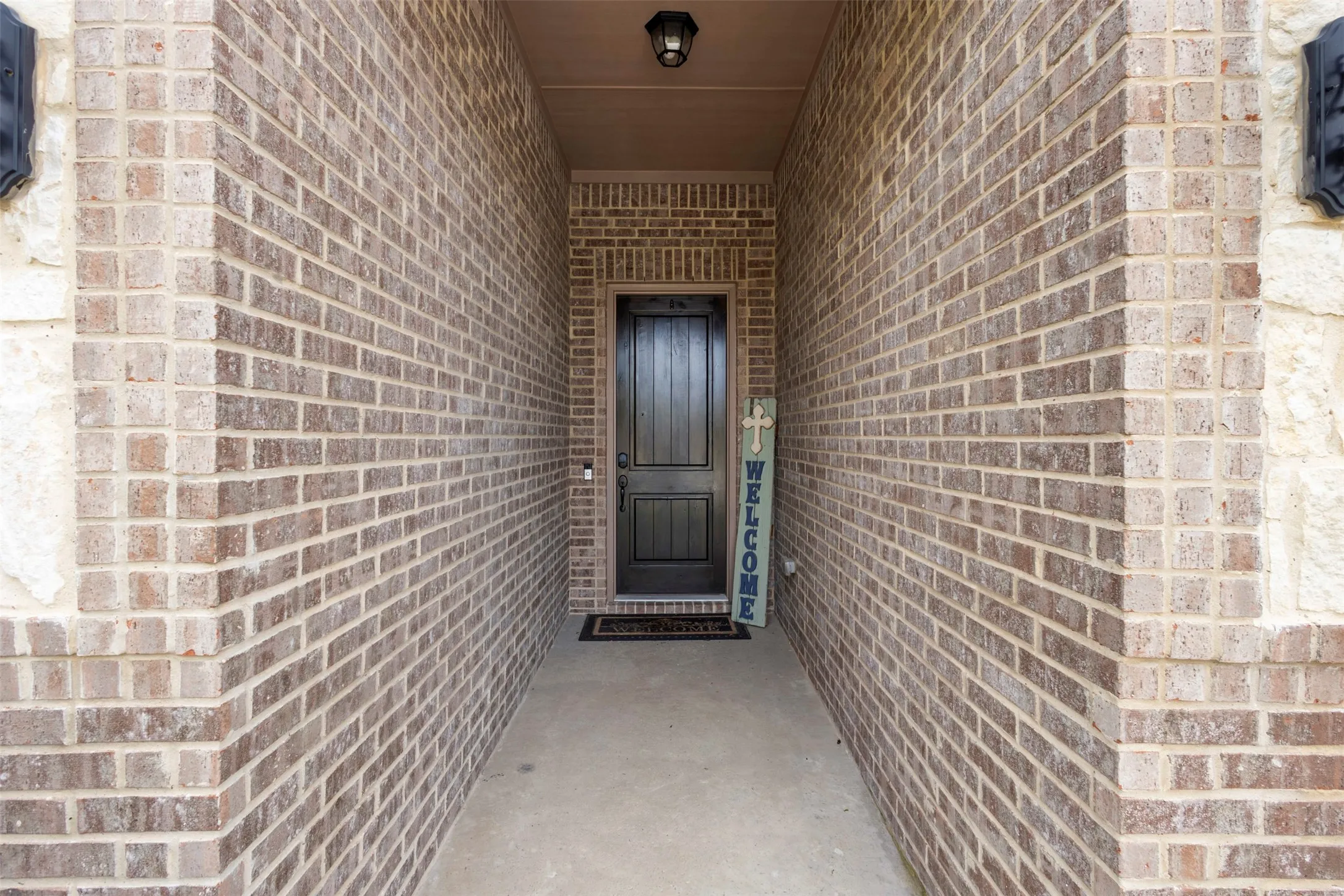 Recessed entry featuring a dark-toned paneled door, brick facade, stone detailing, and a concrete walkway
