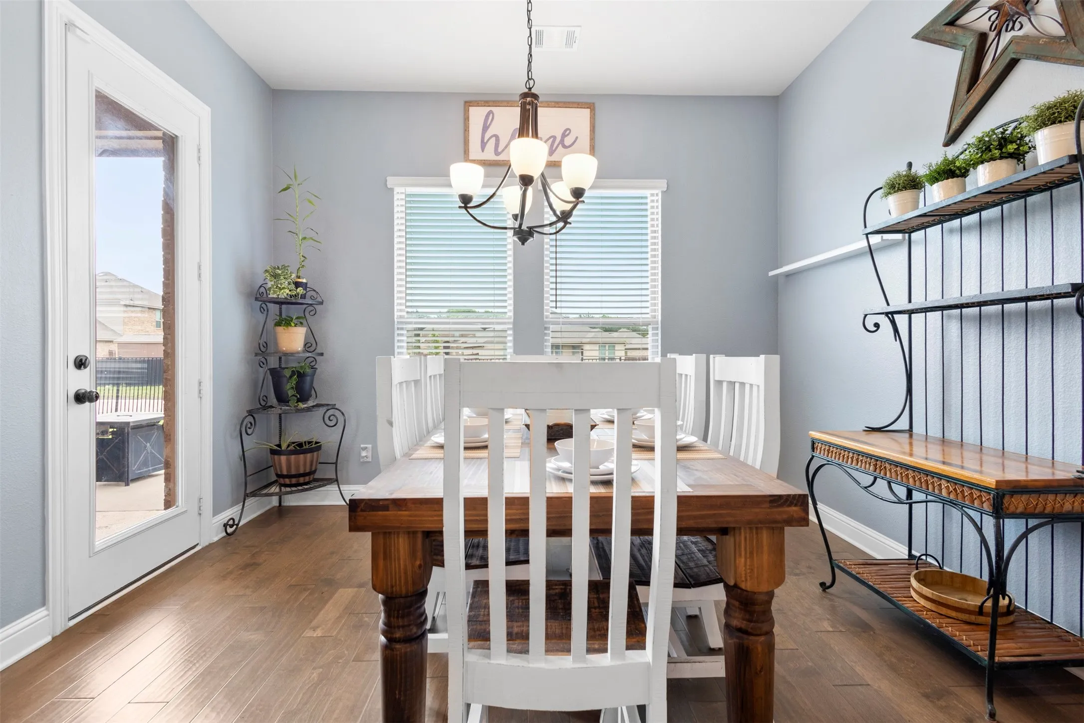 Dining area featuring wood-finish flooring, a white trim glass-paneled door, two windows with blinds, a multi-bulb chandelier, and light gray walls