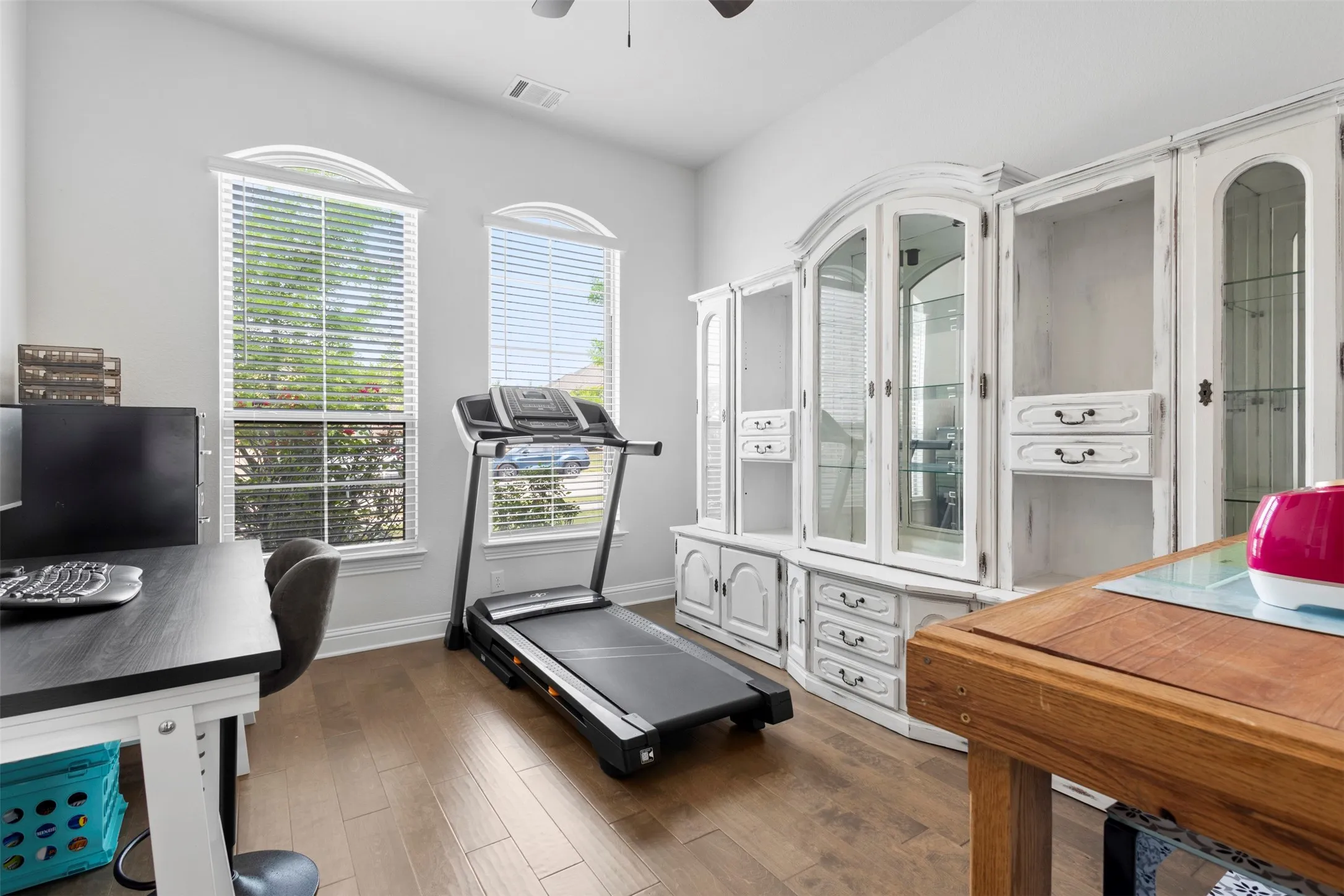Bright room featuring wood-finish flooring, two arched windows with blinds, a ceiling fan, and painted white walls