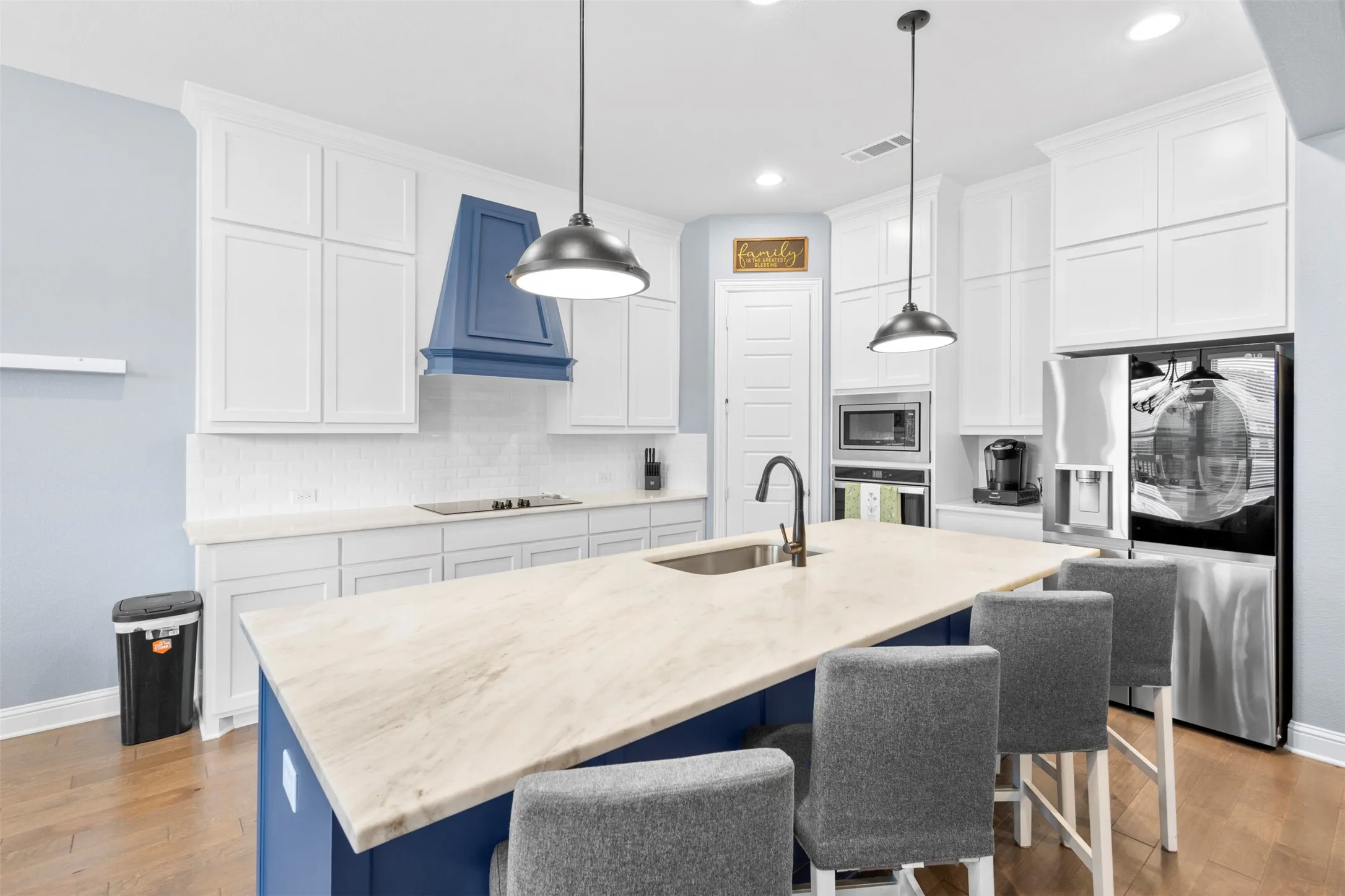 Kitchen featuring a large island with a light-toned countertop, white cabinetry, a built-in microwave, a dark blue range hood, and wood-finish flooring