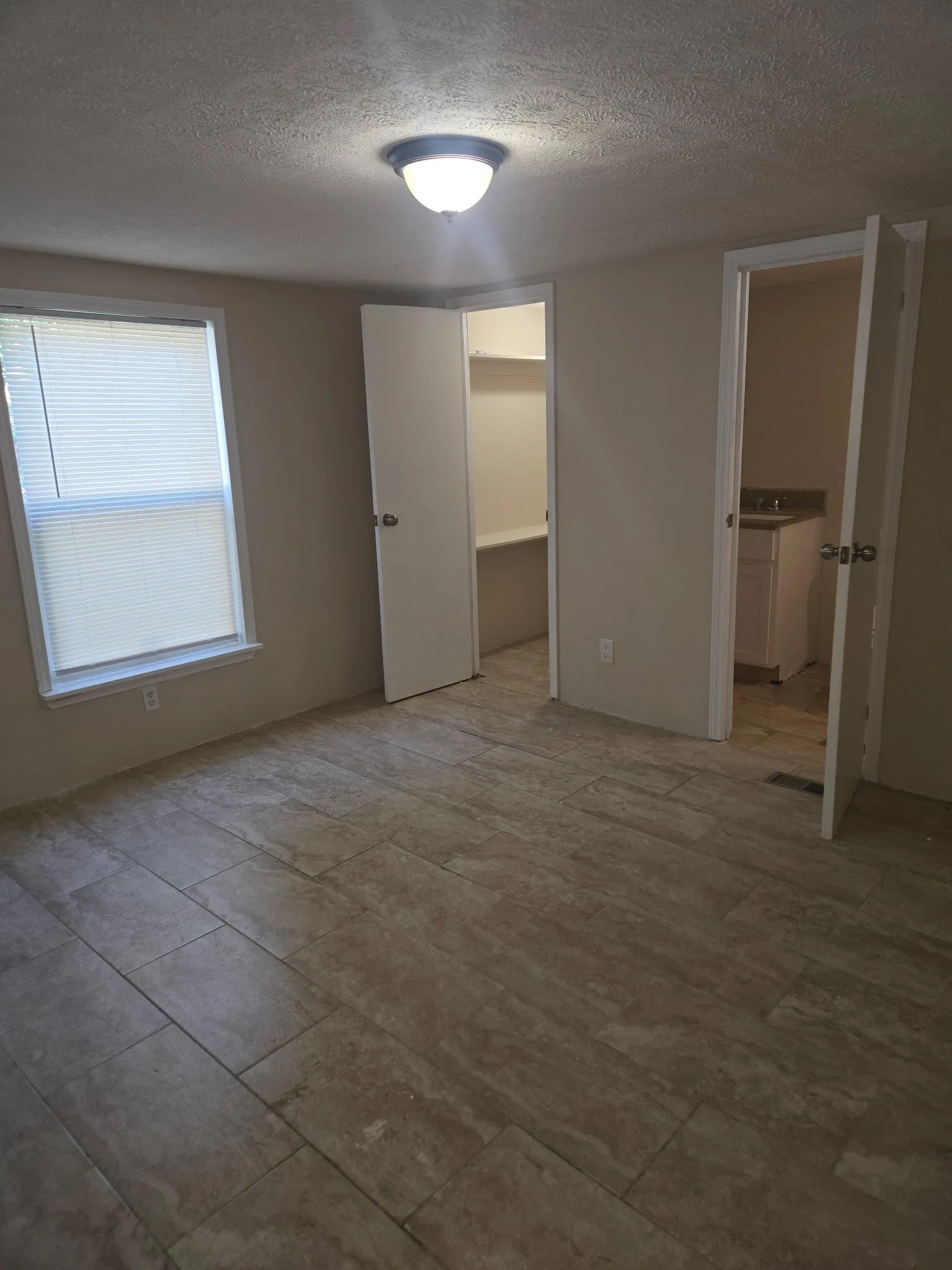 Spacious room featuring large format tile flooring, a window with blinds, and a built-in closet with shelving