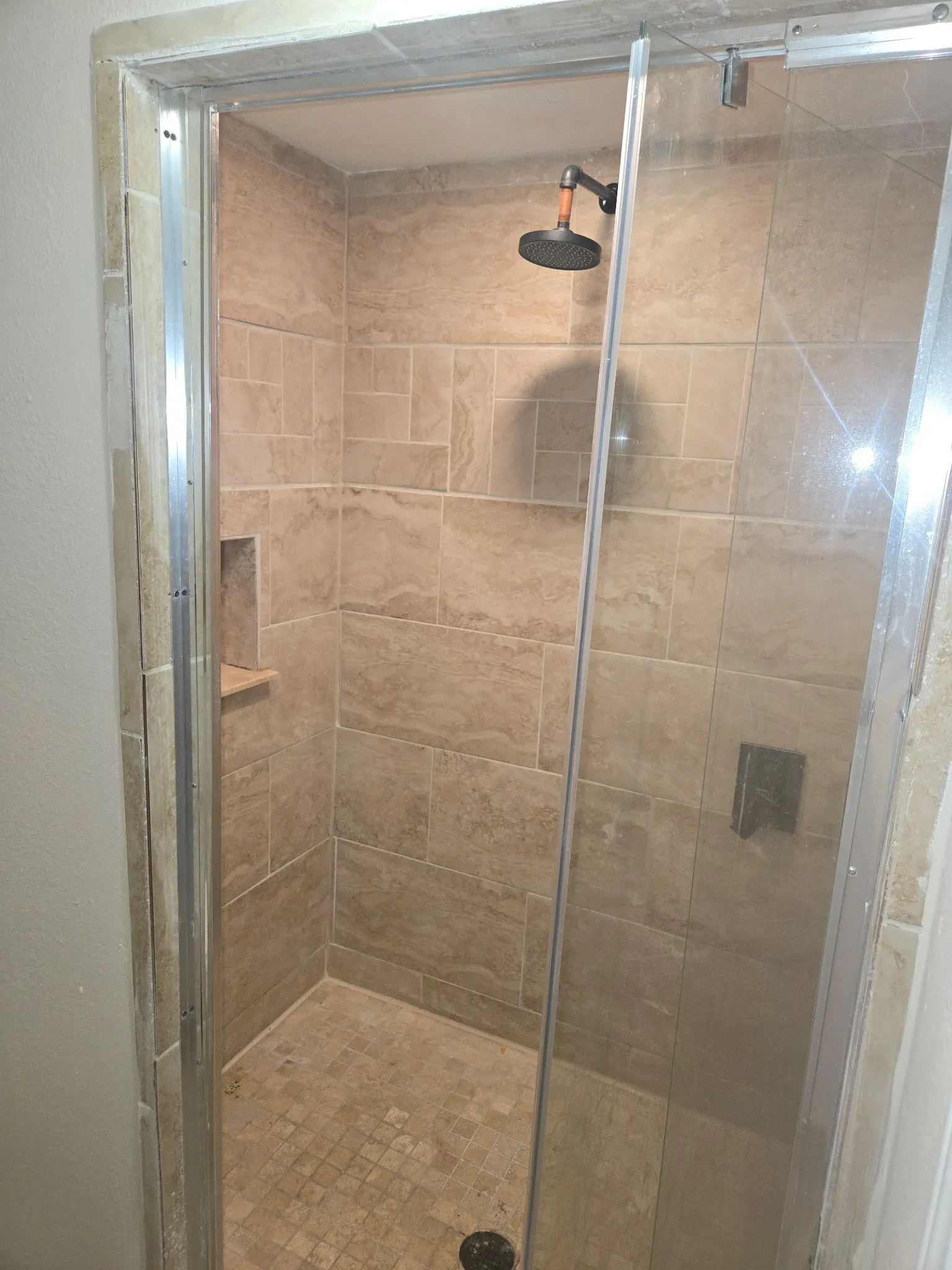Glass-enclosed shower featuring large format tile walls, a mosaic tile floor, and a built-in shower niche