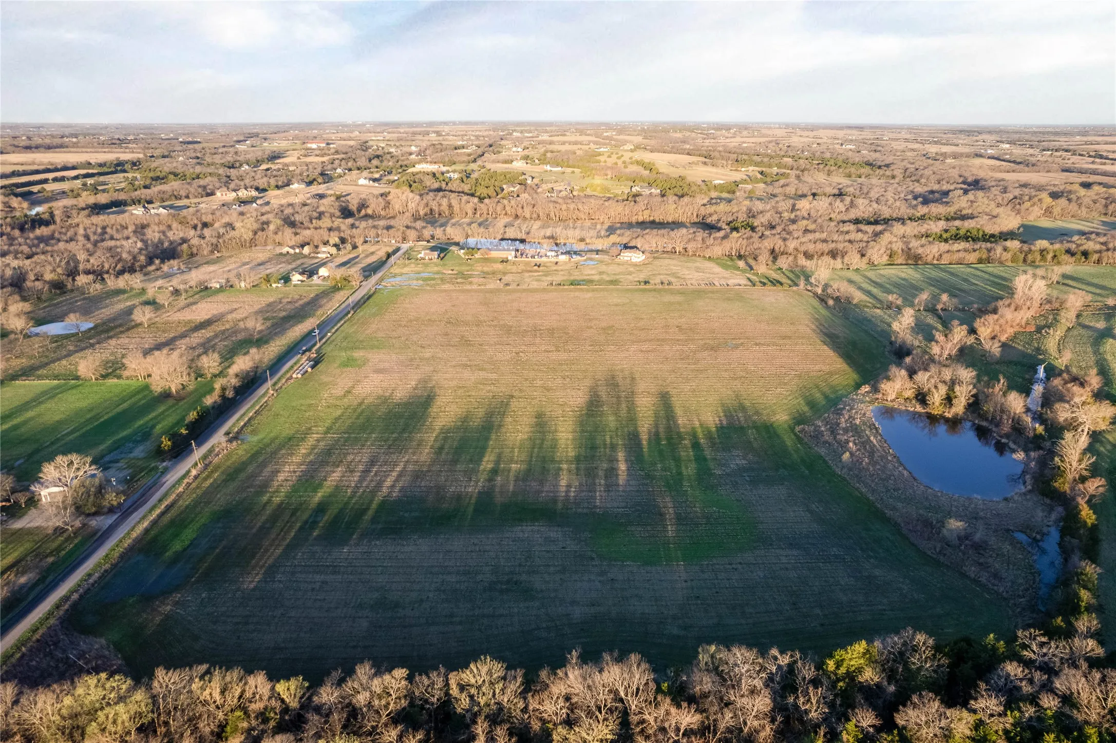 Expansive agricultural land featuring a natural pond and established tree lines