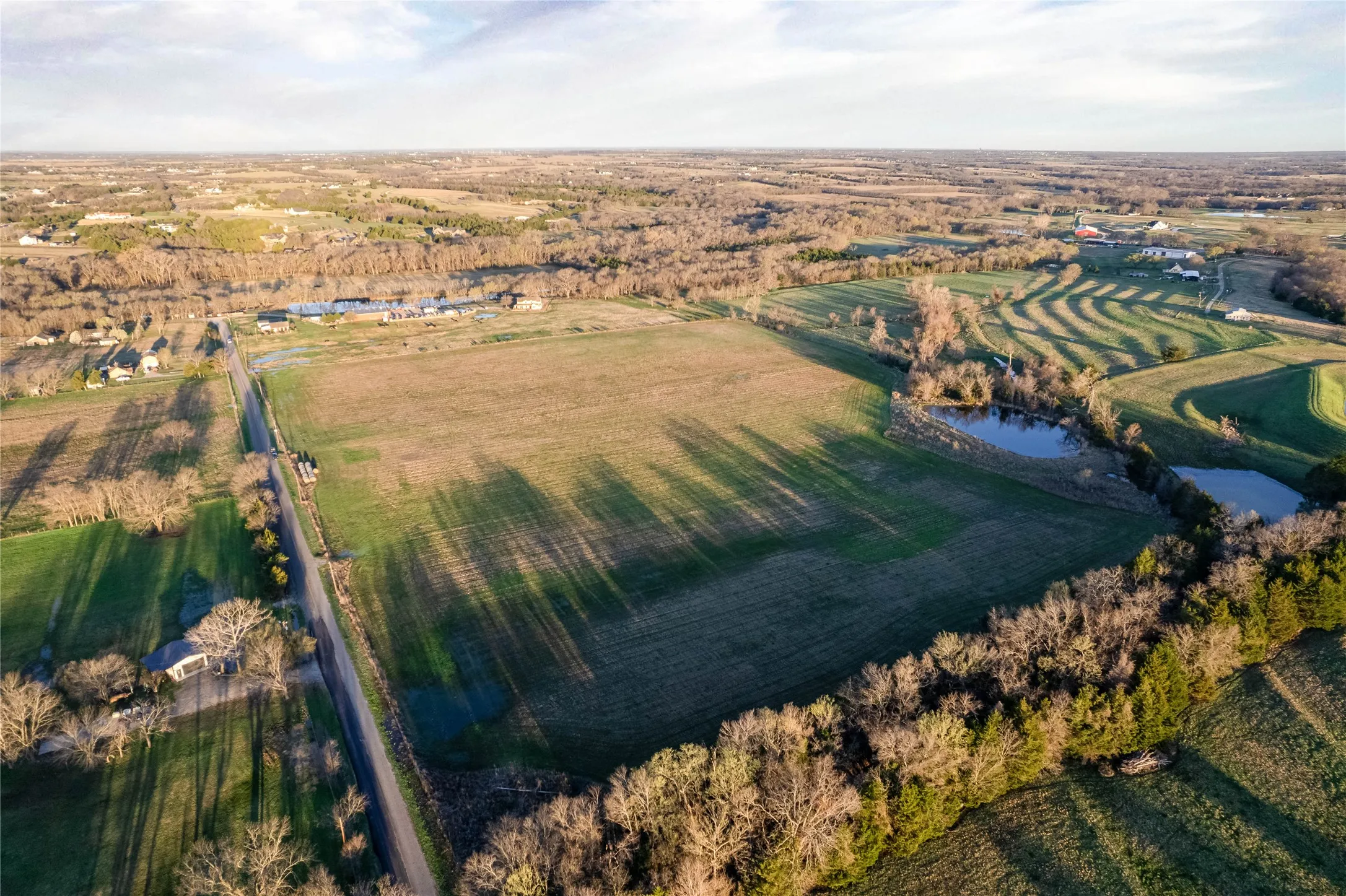 Expansive land parcel featuring open fields, scattered mature trees, and multiple bodies of water