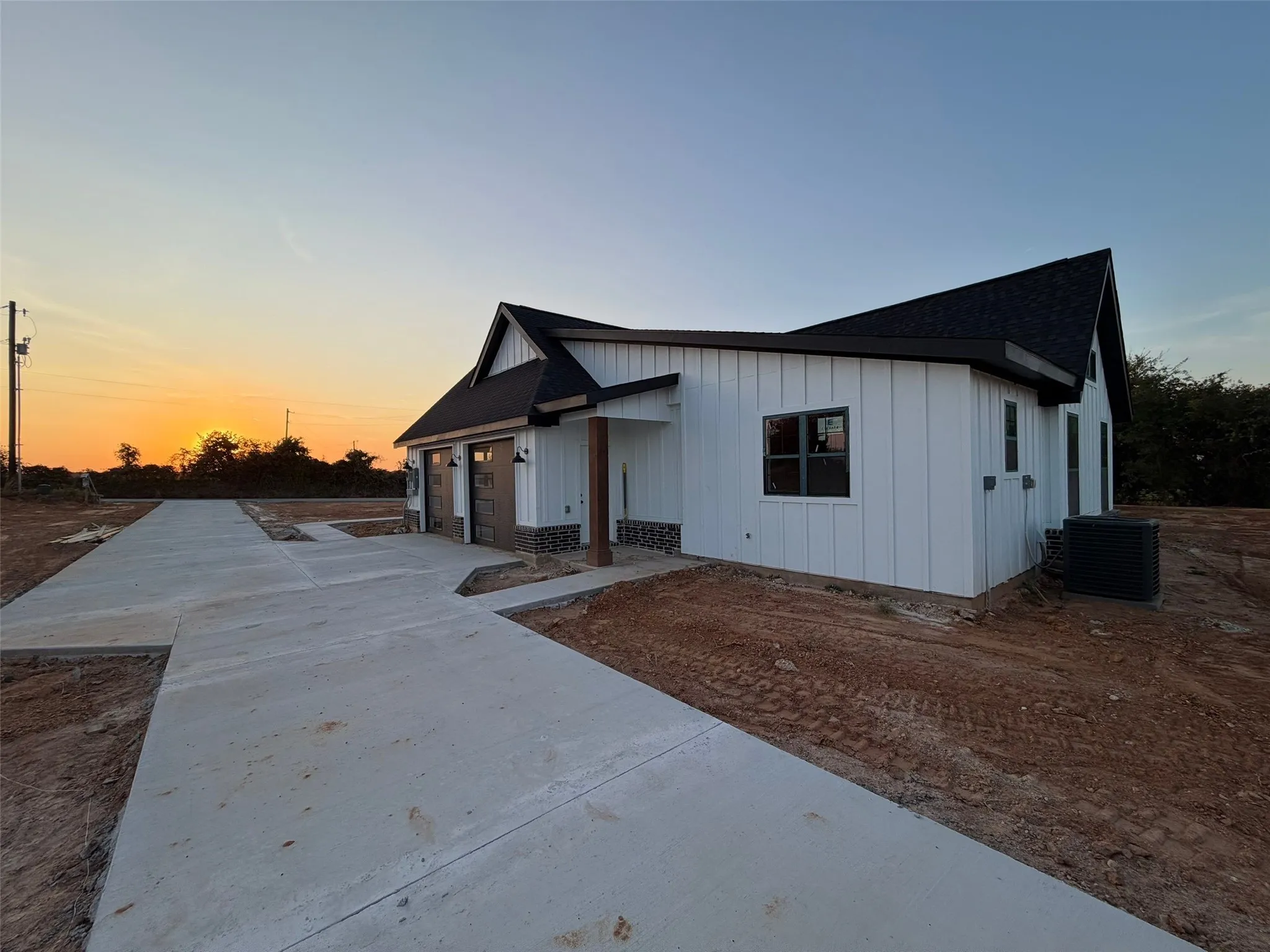 Exterior featuring white vertical siding, black-framed windows, a dark shingle roof, a concrete driveway, and an attached two-car garage with overhead doors