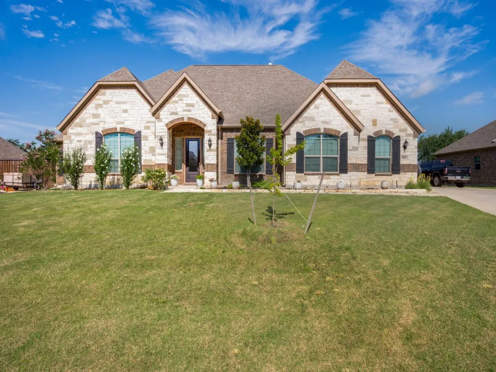Elegant stone-and-brick home with striking curb appeal, manicured landscaping, expansive front lawn, and a welcoming covered front porch entry beneath soaring gabled rooflines