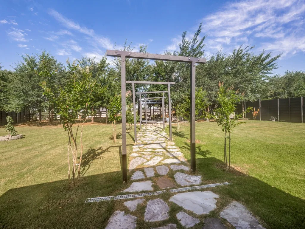 A charming stone pathway leads beneath a series of modern pergola-style arches creating an inviting garden promenade that leads to the outdoor living space