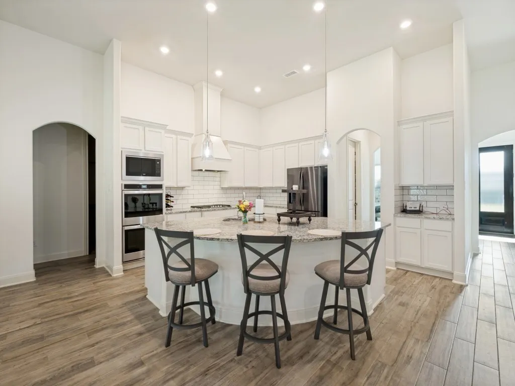 You can easily see how this kitchen is the heart of this home. Curved breakfast bar is breathtaking.  Island gives you plenty of room for prepping and serving.  Perfect little nook for a coffee bar to the right. Double ovens plus a microwave to the left. Lots of lighting, stylish subway tile and tons of cabinet storage. Arched doorway to the right of the fridge leads to the butler's pantry on the right and to the walk-iin pantry on the left.