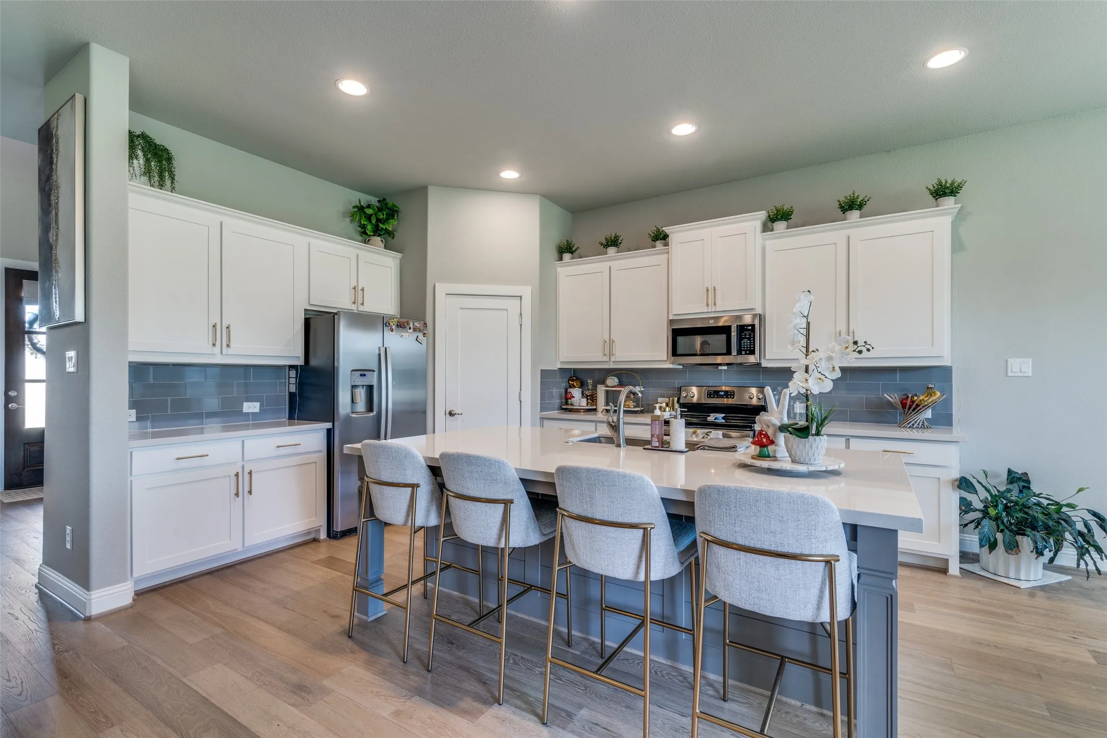 Expansive kitchen featuring a large central island, light wood-finish flooring, white cabinetry, integrated stainless steel appliances, and subway tile backsplash