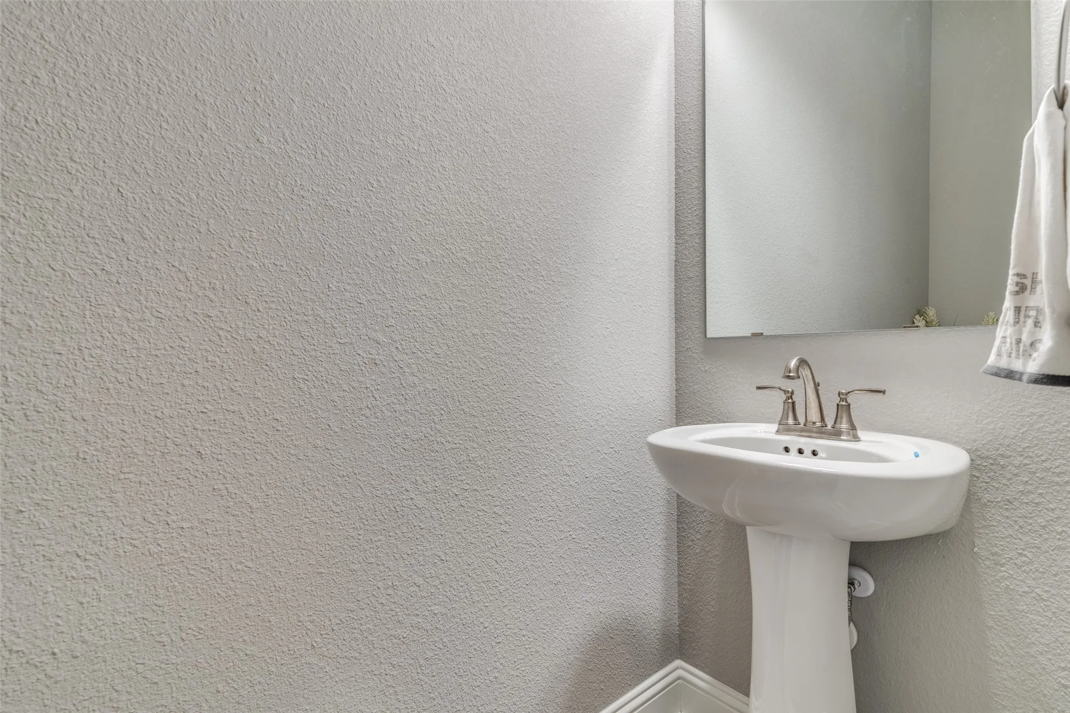 Pedestal sink with brushed nickel faucet, set against textured walls