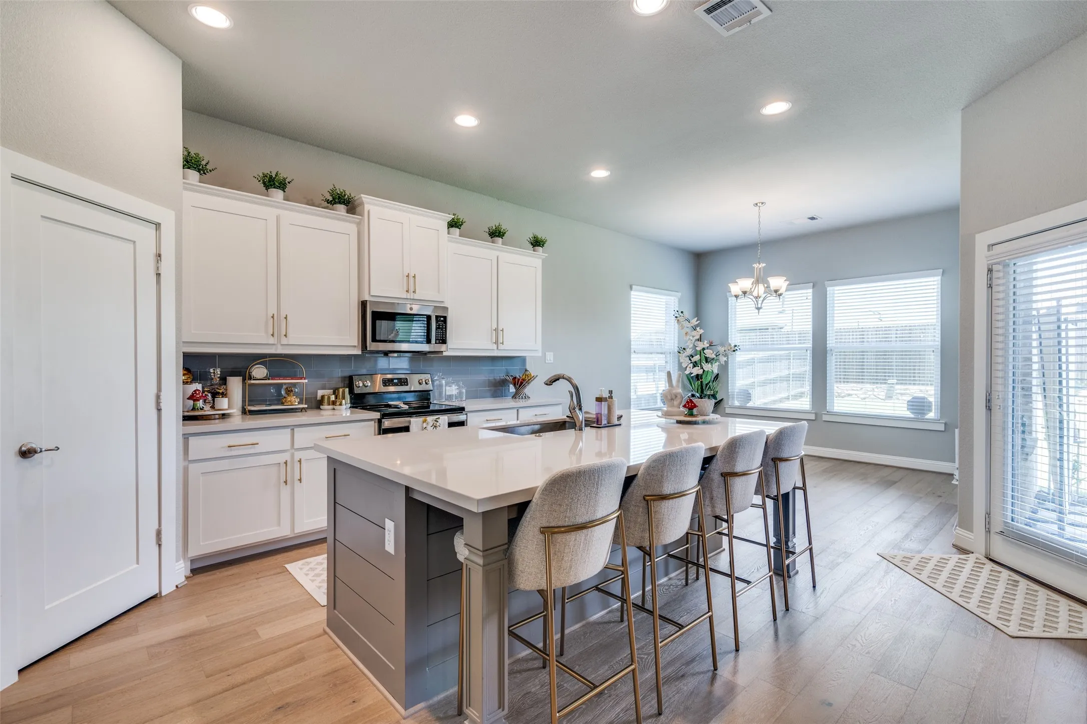Spacious kitchen featuring an extended island with a quartz countertop, stainless steel appliances, white cabinetry, and wood-finish flooring