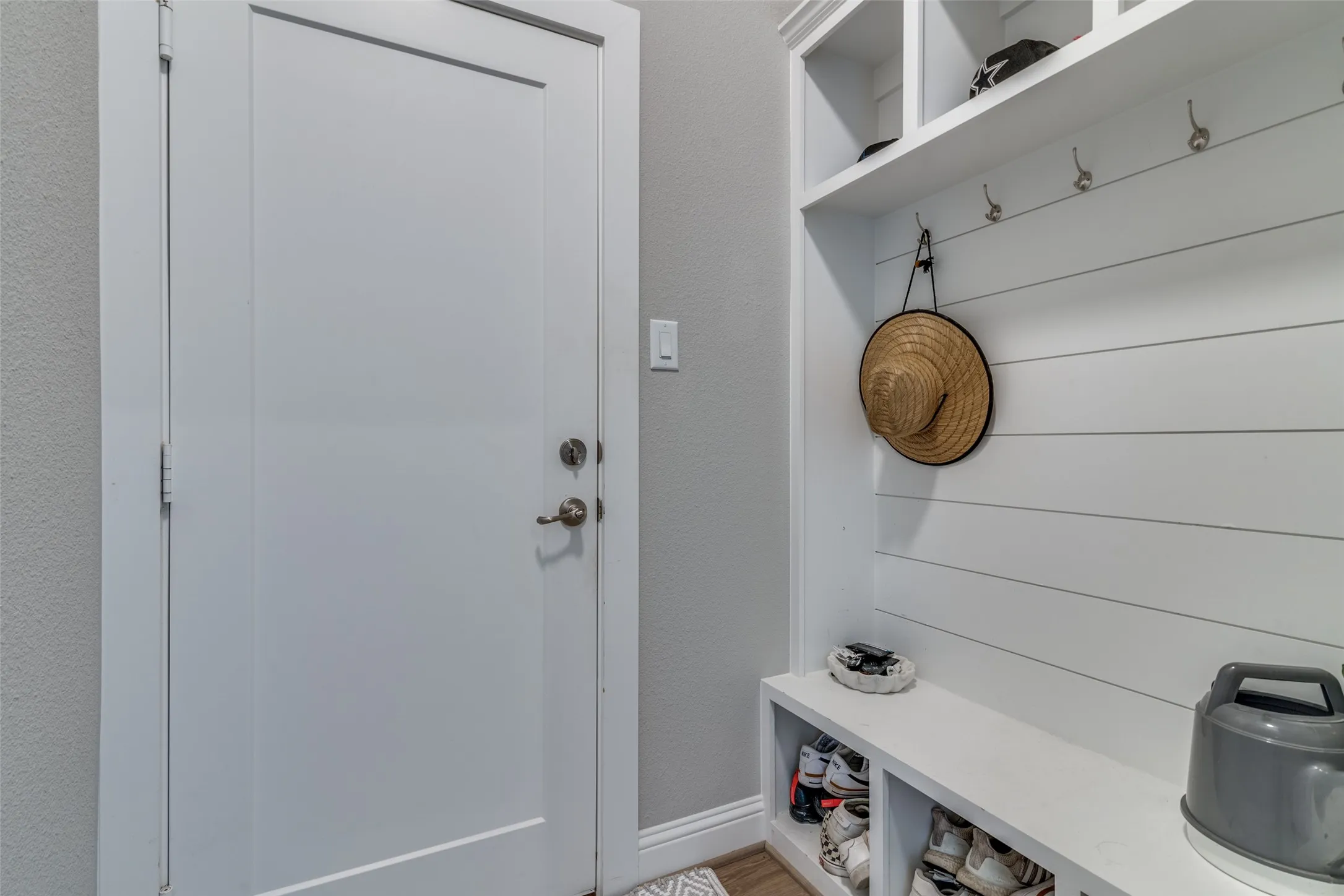 Entryway mudroom featuring built-in storage with open shelving, integrated bench seating, shoe cubbies, and wall-mounted coat hooks