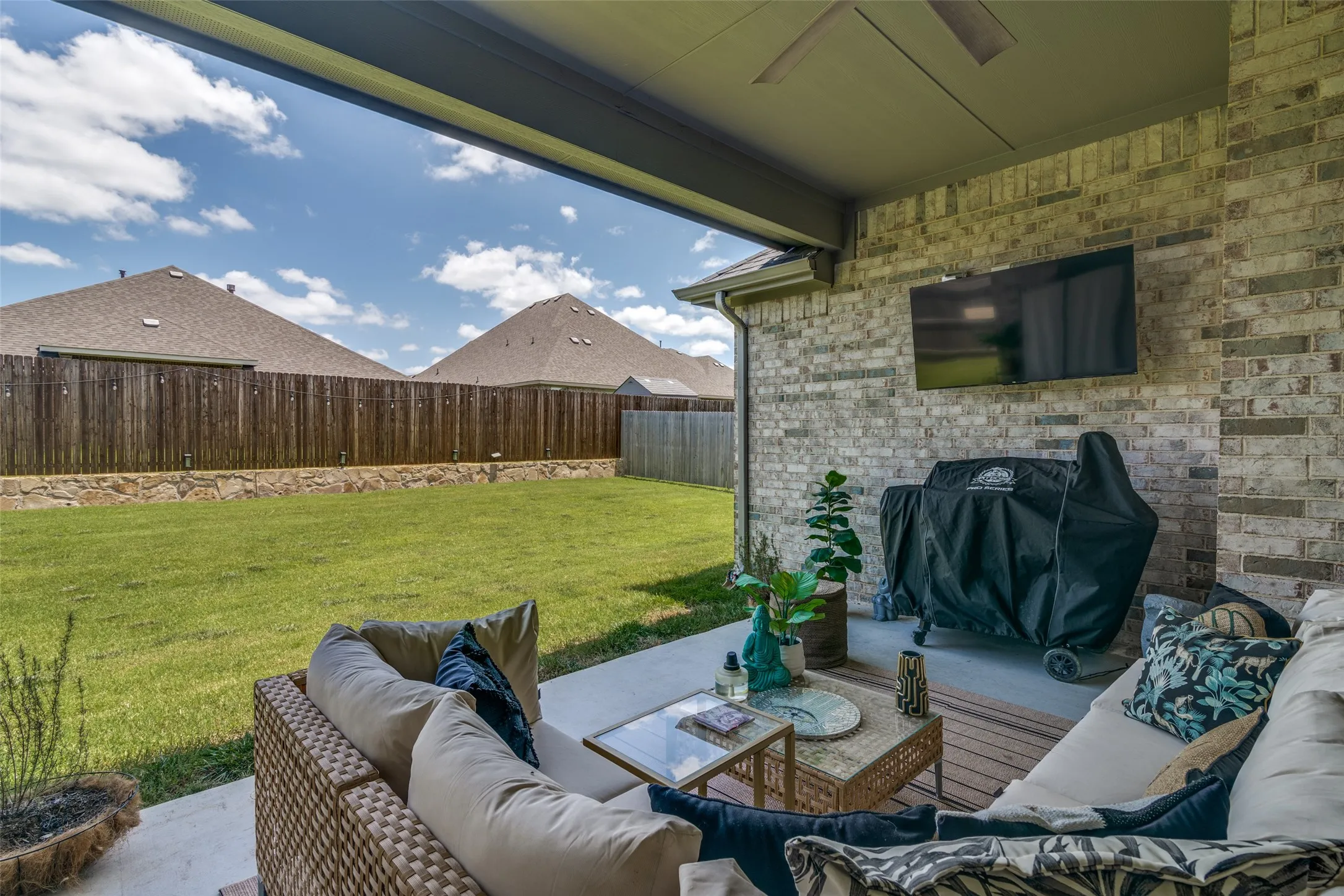 Covered patio featuring a ceiling fan, mounted television, and brick exterior wall