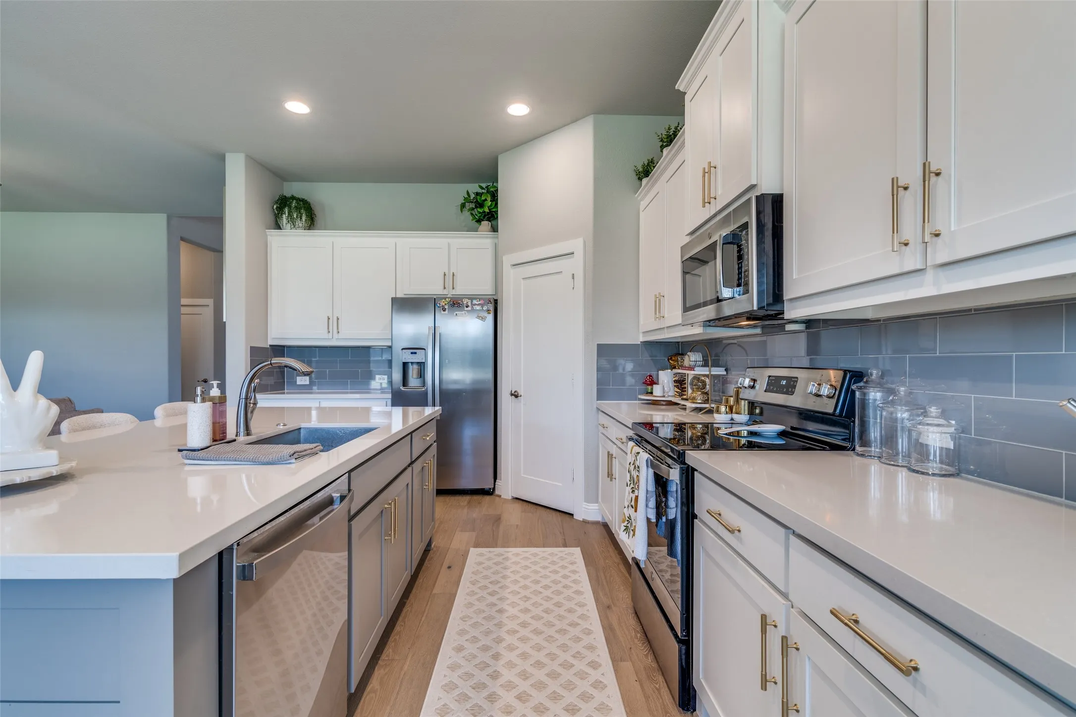 Modern kitchen featuring a large island with an undermount sink, stainless steel appliances, light wood-finish flooring, white shaker cabinetry, and a gray subway tile backsplash