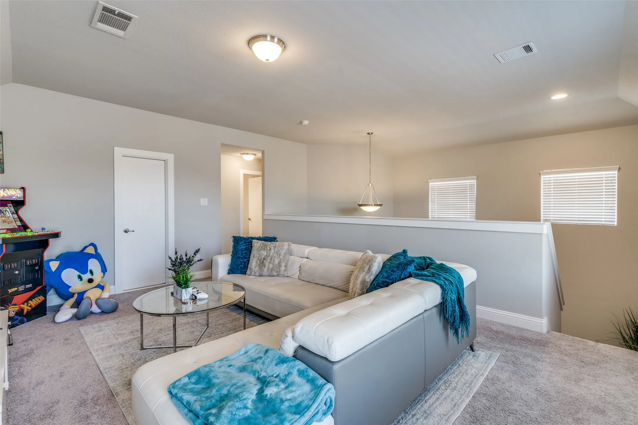 Spacious loft area featuring neutral carpeting, a partial wall with white trim, and multiple windows with blinds
