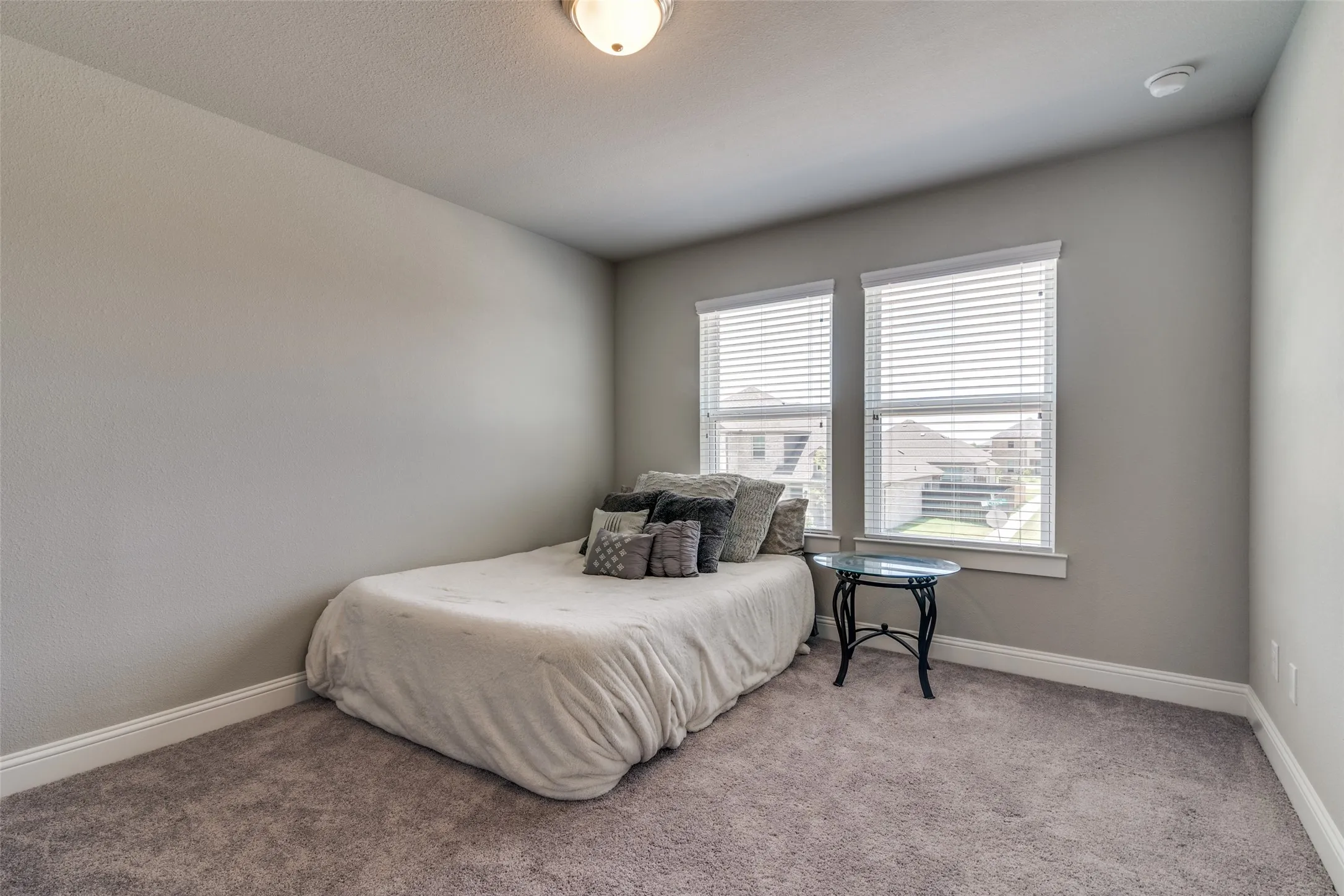 Carpeted room featuring two windows with white blinds, neutral wall paint, white baseboards, and a flush mount ceiling light
