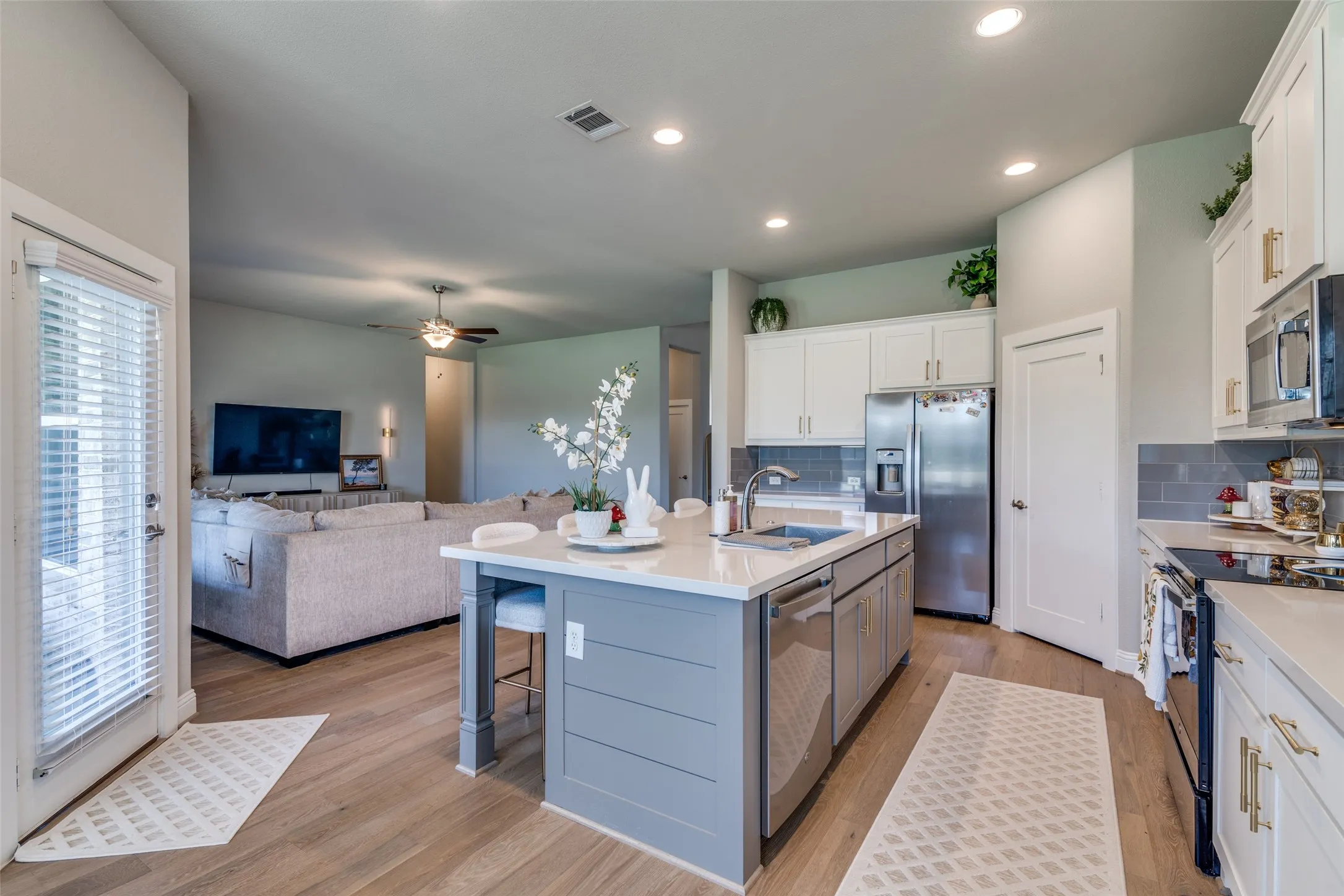 Open-concept kitchen featuring white cabinetry, stainless steel appliances, light-toned wood-finish flooring, a light gray subway tile backsplash, and a central island with a white countertop and shiplap paneling