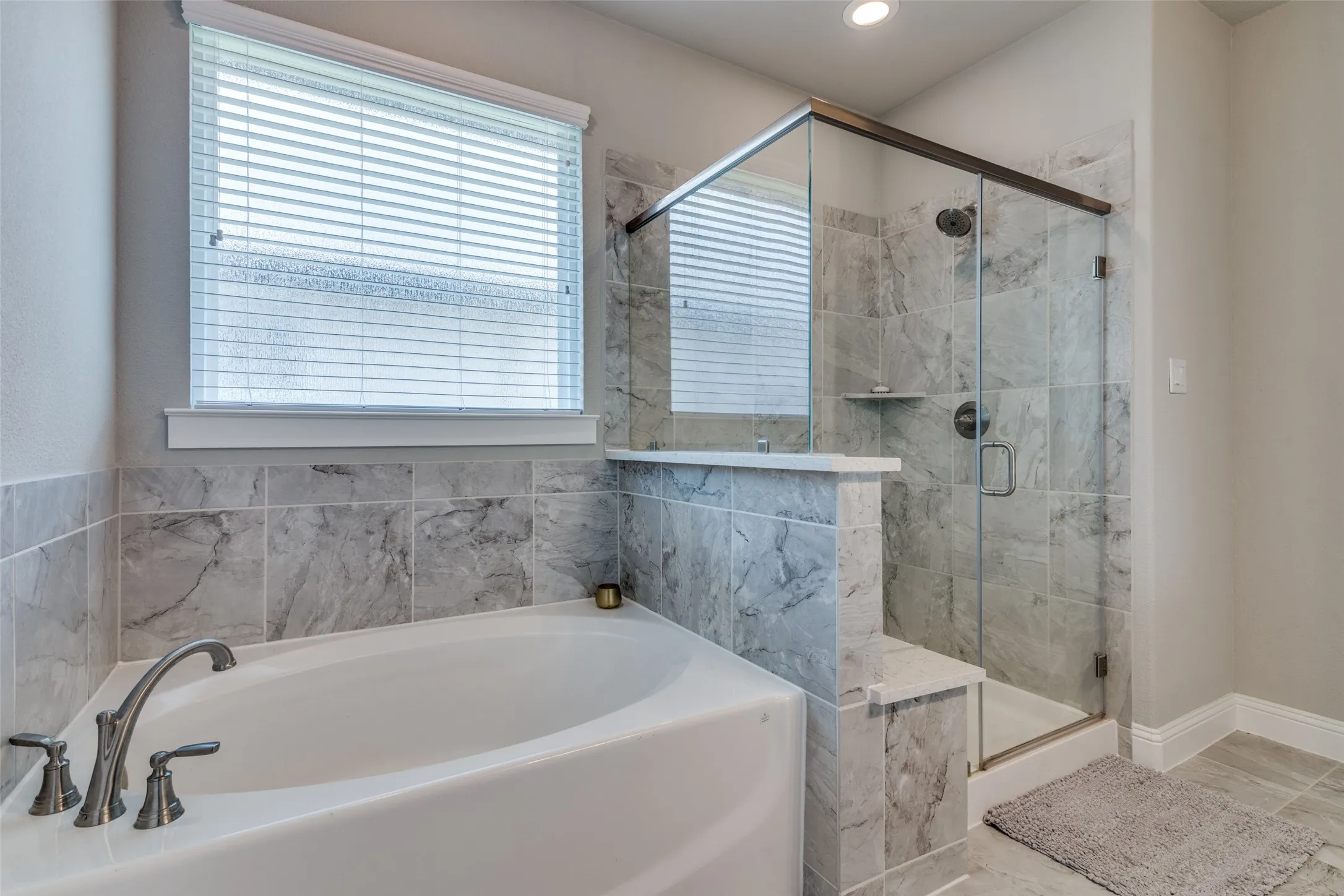 Soaking tub with brushed nickel fixtures, surrounded by large format light grey stone-look tile