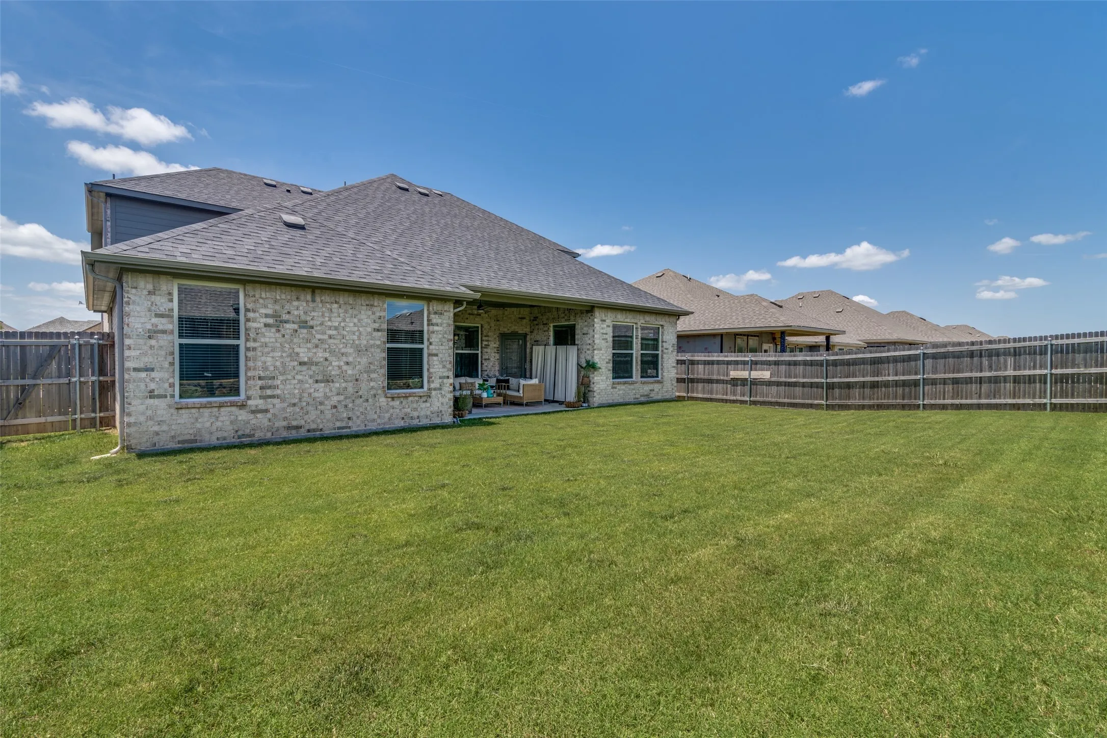 Expansive backyard featuring a manicured lawn, full perimeter wood fencing, and a covered patio area