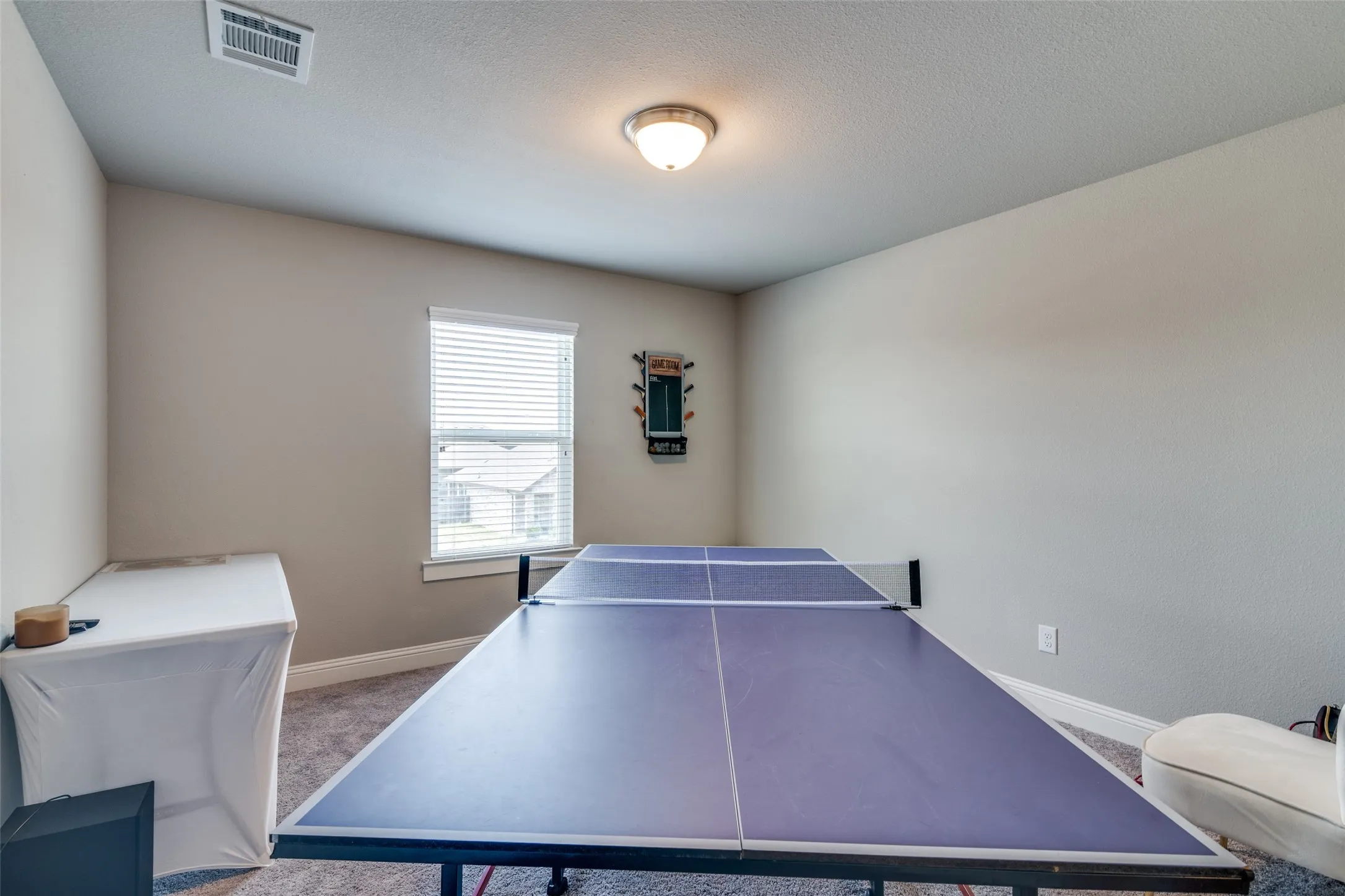 Spacious room featuring neutral painted walls, textured carpet flooring, and a single window with horizontal blinds