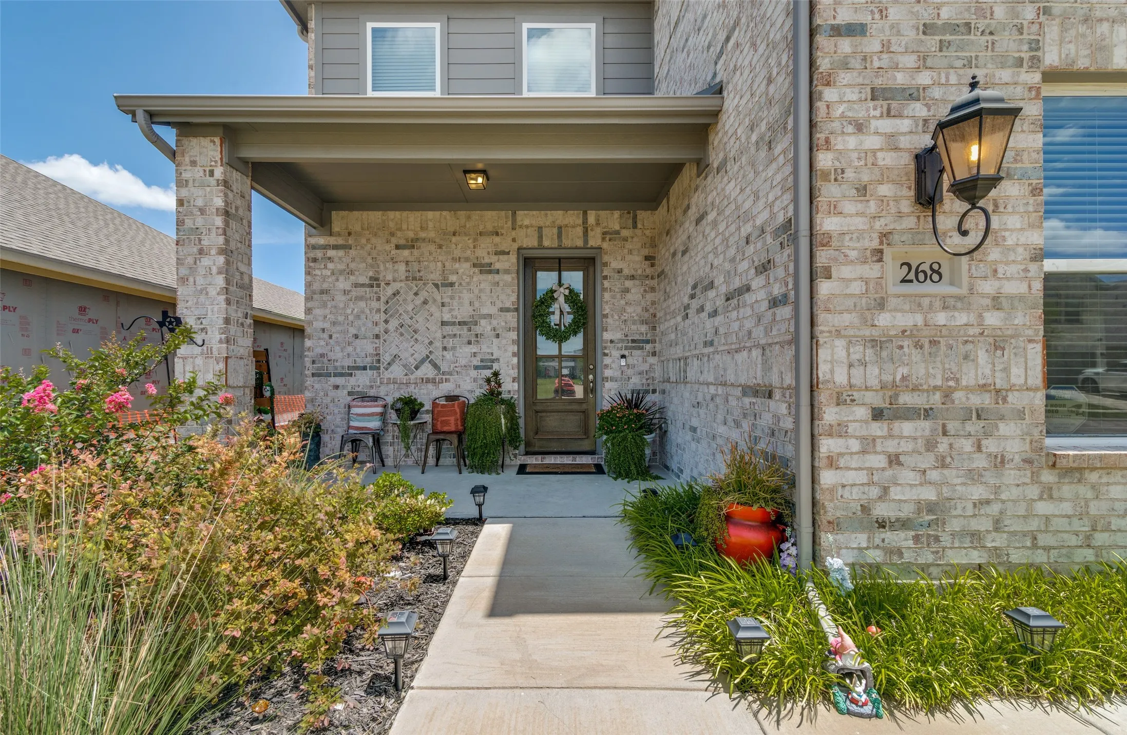 Brick facade home featuring a covered front porch, concrete pathway, and landscaping with mature plantings