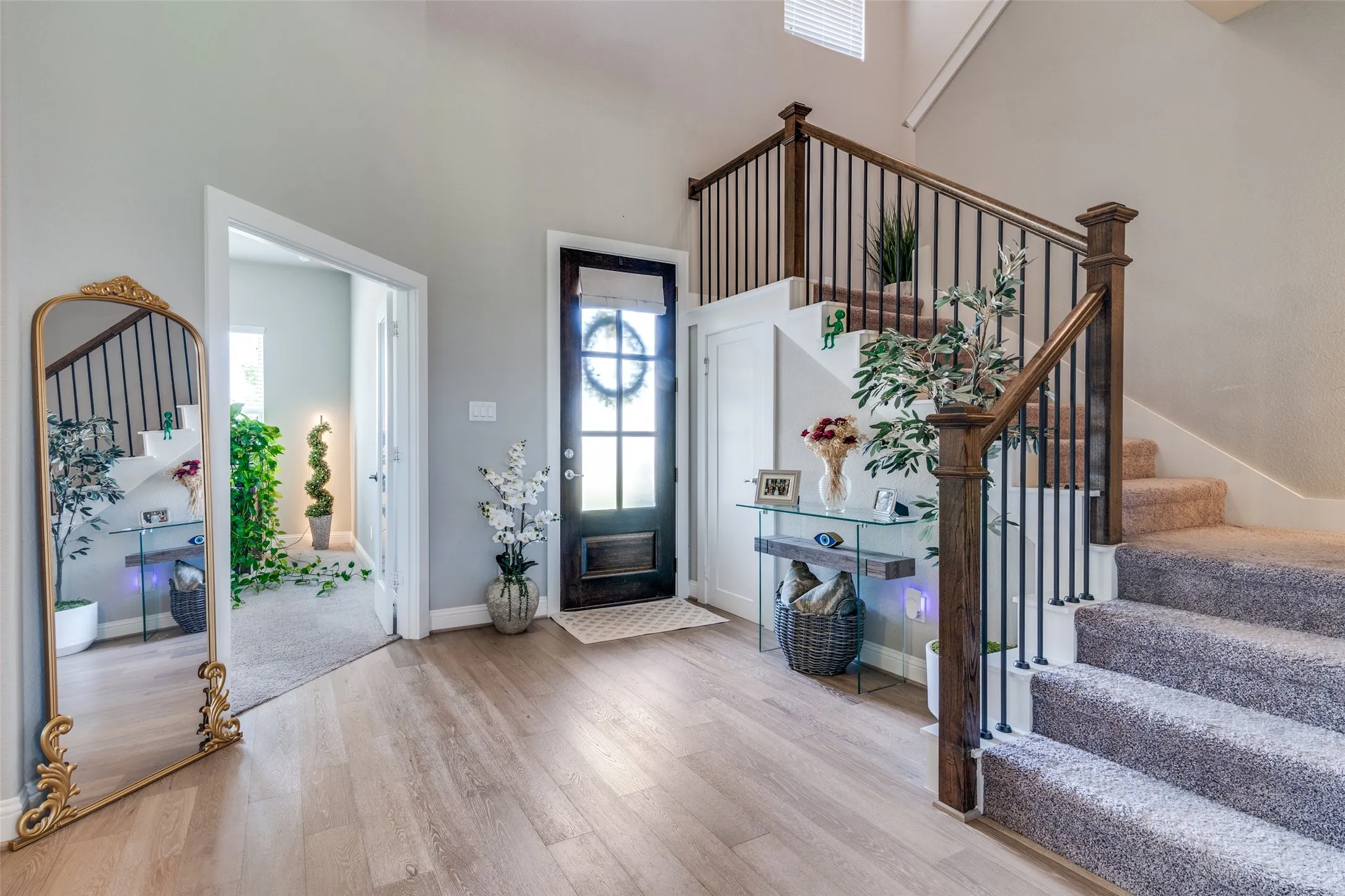 Entryway featuring wood-finish flooring, a dark wood front door with glass panels, and a staircase with carpeted treads and dark wood newel posts with black metal balusters