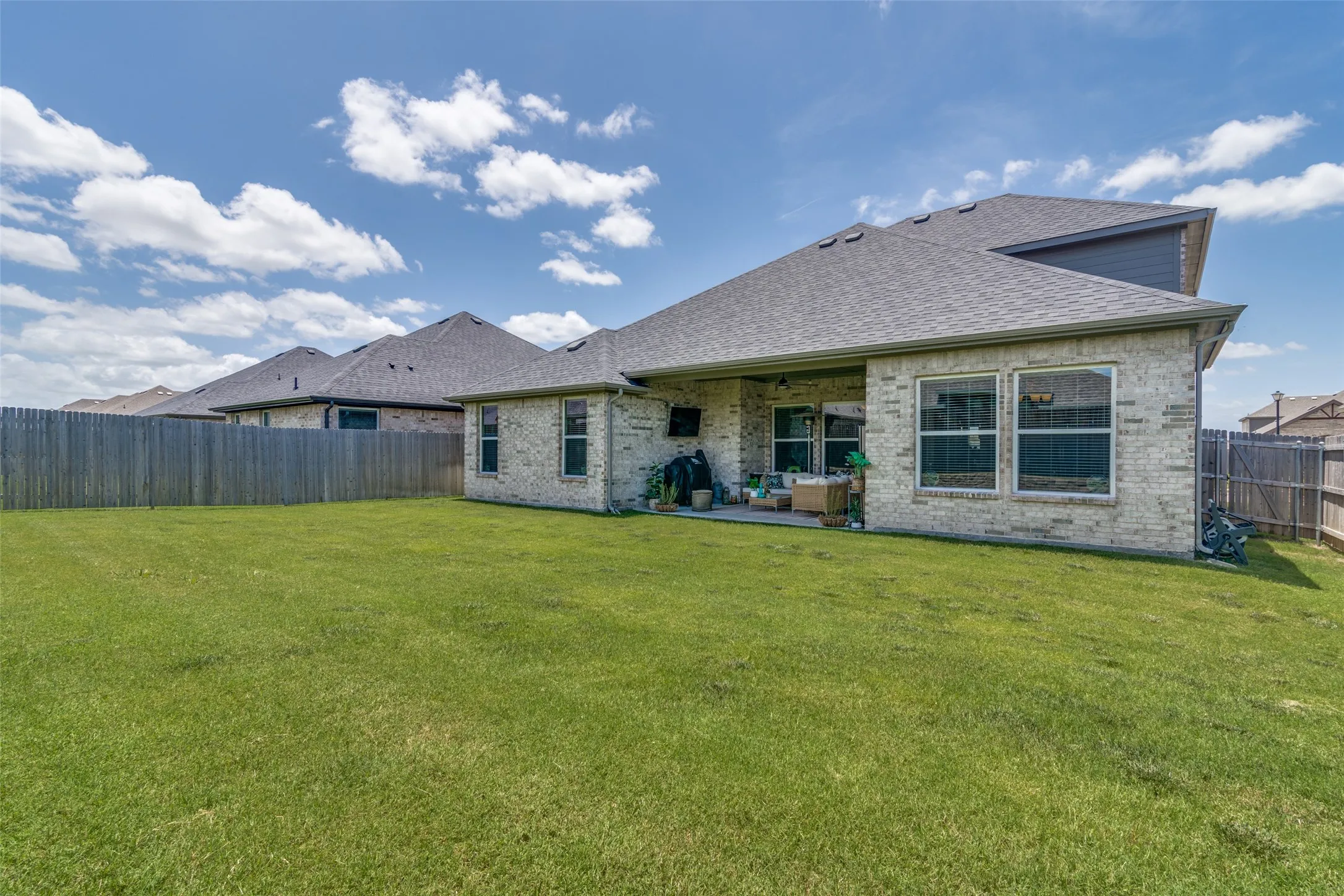 Expansive backyard featuring a manicured lawn, full privacy fencing, and a covered patio area