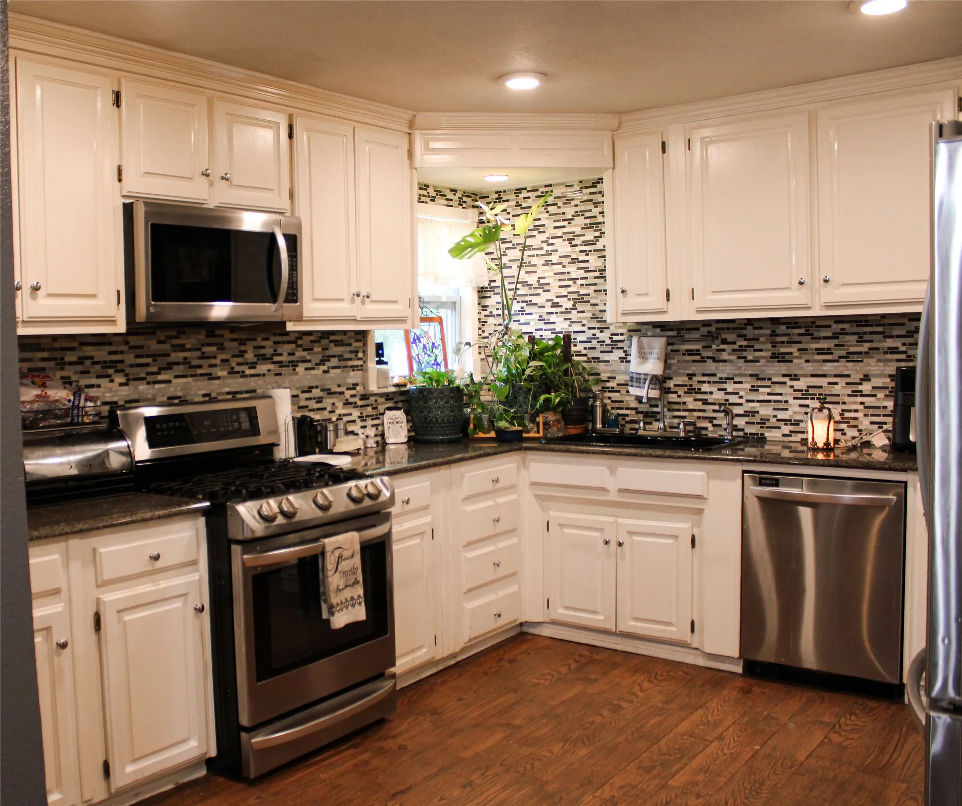 Kitchen featuring white cabinetry, dark countertops, a mosaic tile backsplash, stainless steel appliances, and wood-finish flooring