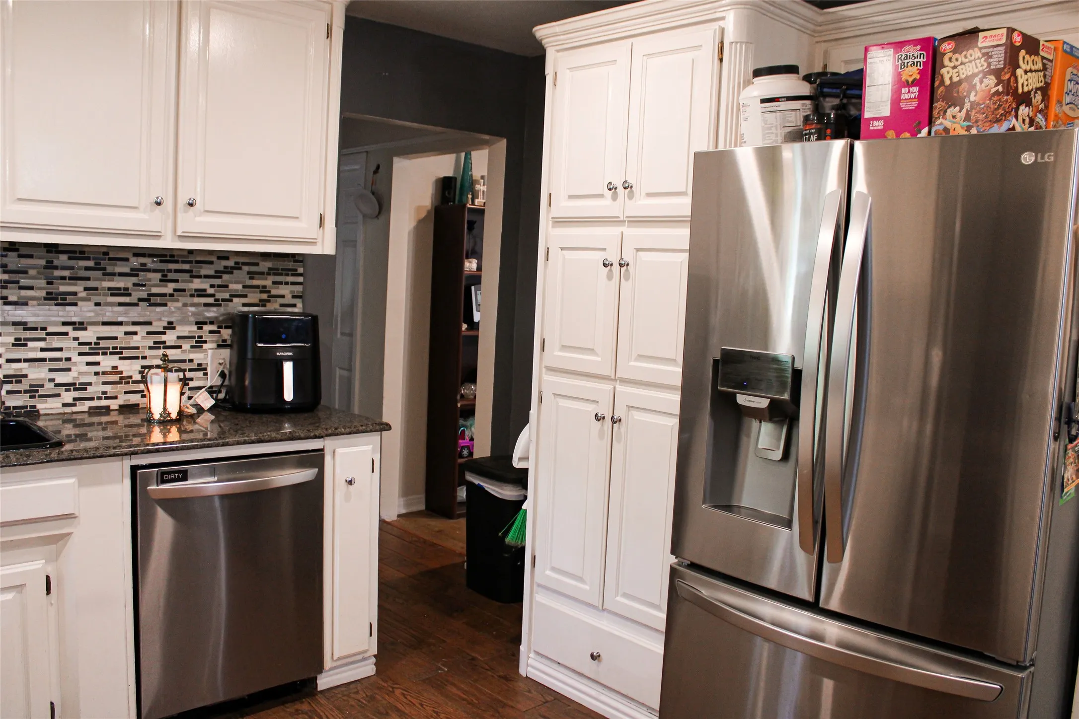 Kitchen featuring white cabinetry, dark wood-finish flooring, a mosaic tile backsplash, and stainless steel appliances including a refrigerator and dishwasher