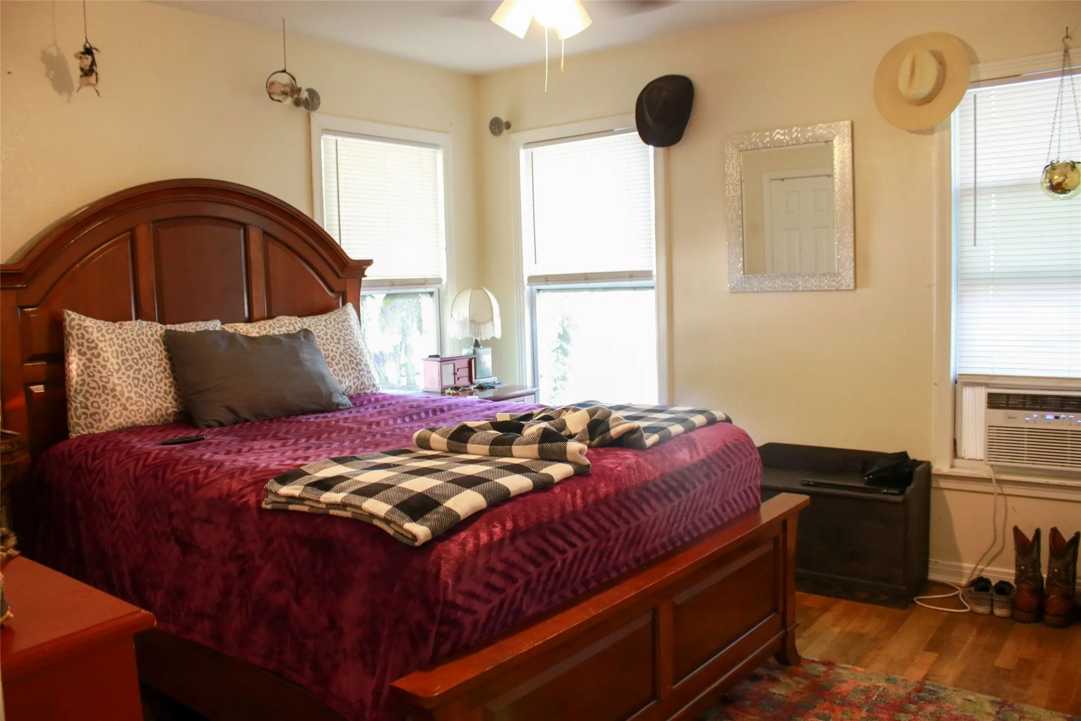 Hardwood-style flooring with a built-in wall-mounted air conditioning unit, ceiling fan, and multiple windows with blinds