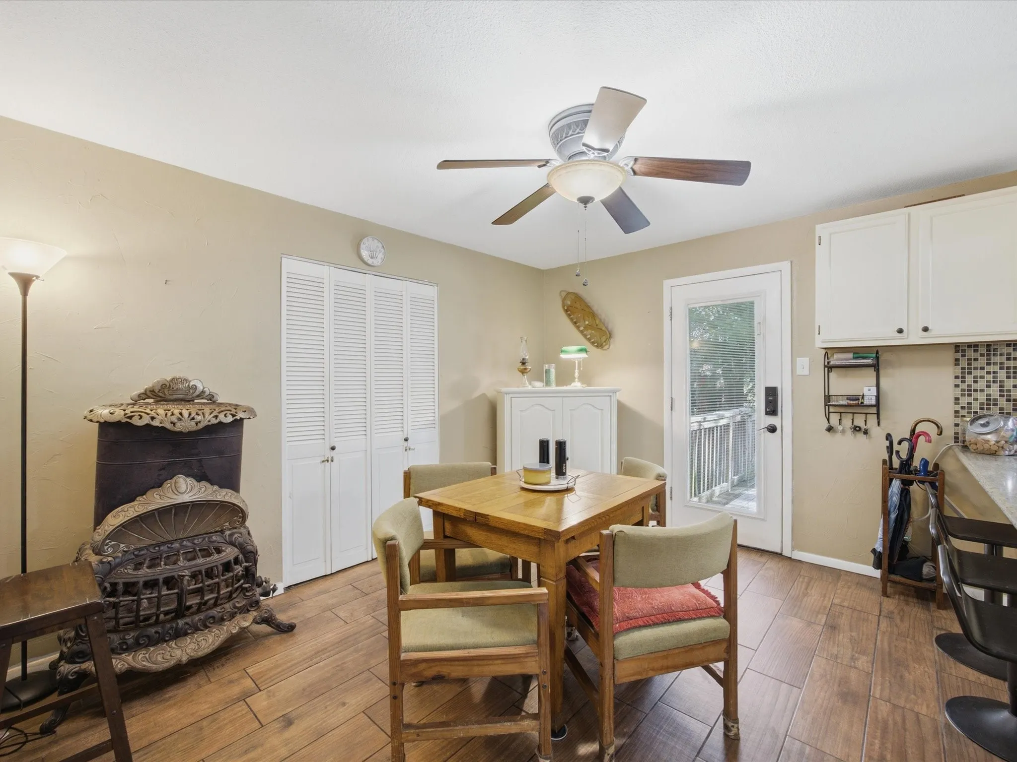 Open-concept dining area featuring wood-finish flooring, a ceiling fan with light fixture, and a white paneled door providing outdoor access