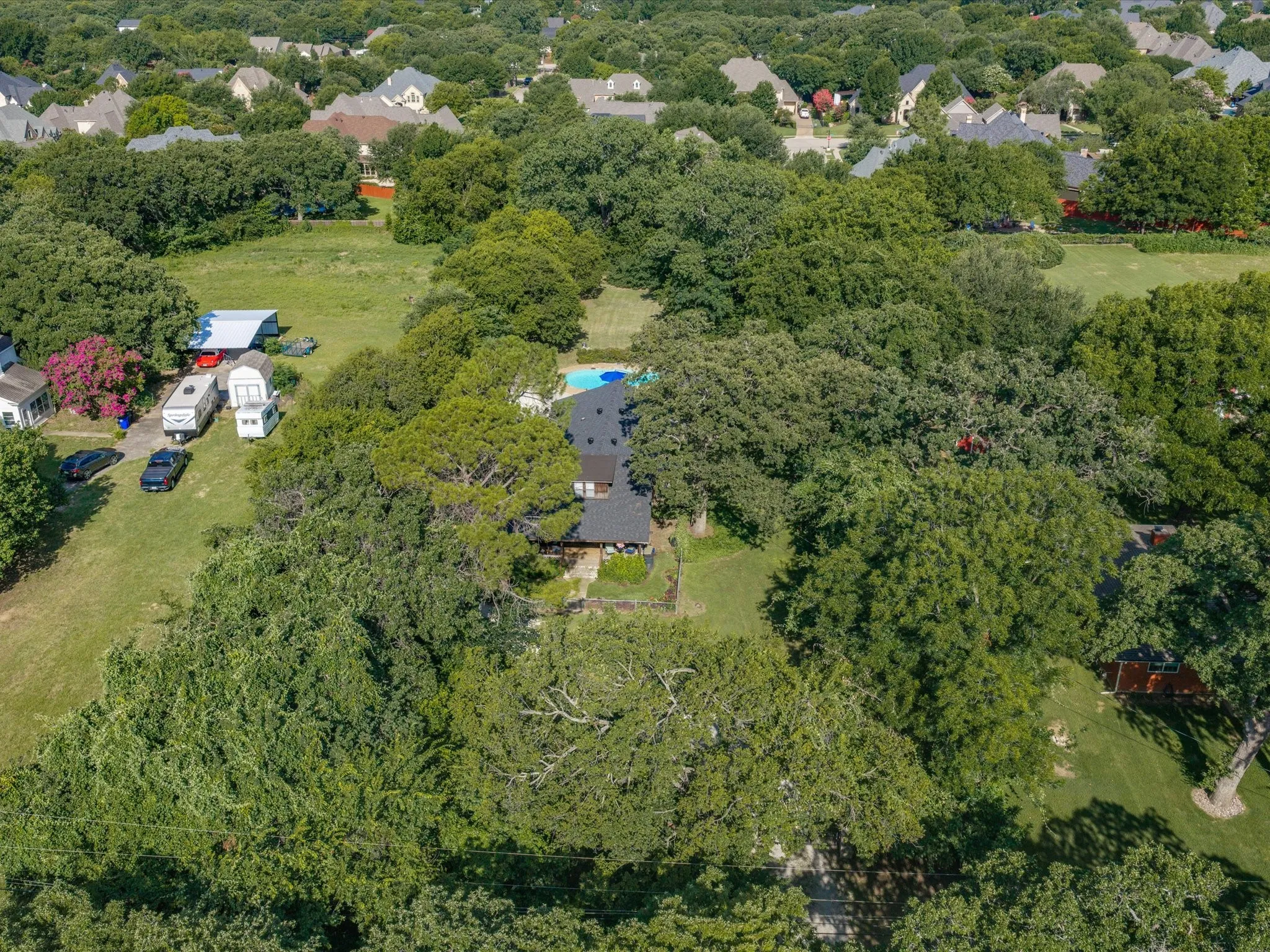 Aerial overview showcasing a property featuring a dark-roofed residence, a blue-tiled swimming pool, and extensive mature tree coverage