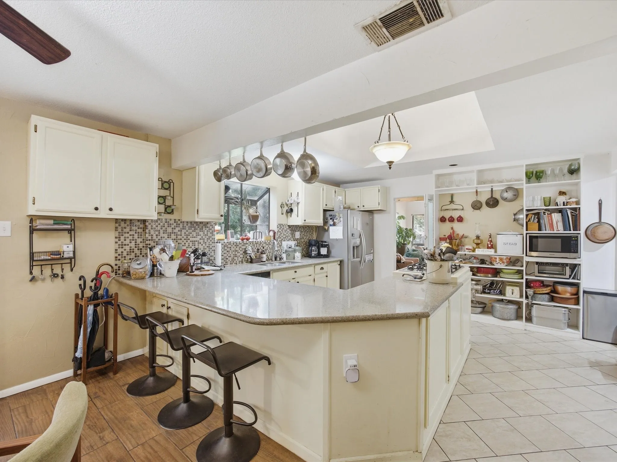 Kitchen featuring an oversized U-shaped counter with seating, white cabinetry, a mosaic tile backsplash, stainless steel appliances, and tile flooring