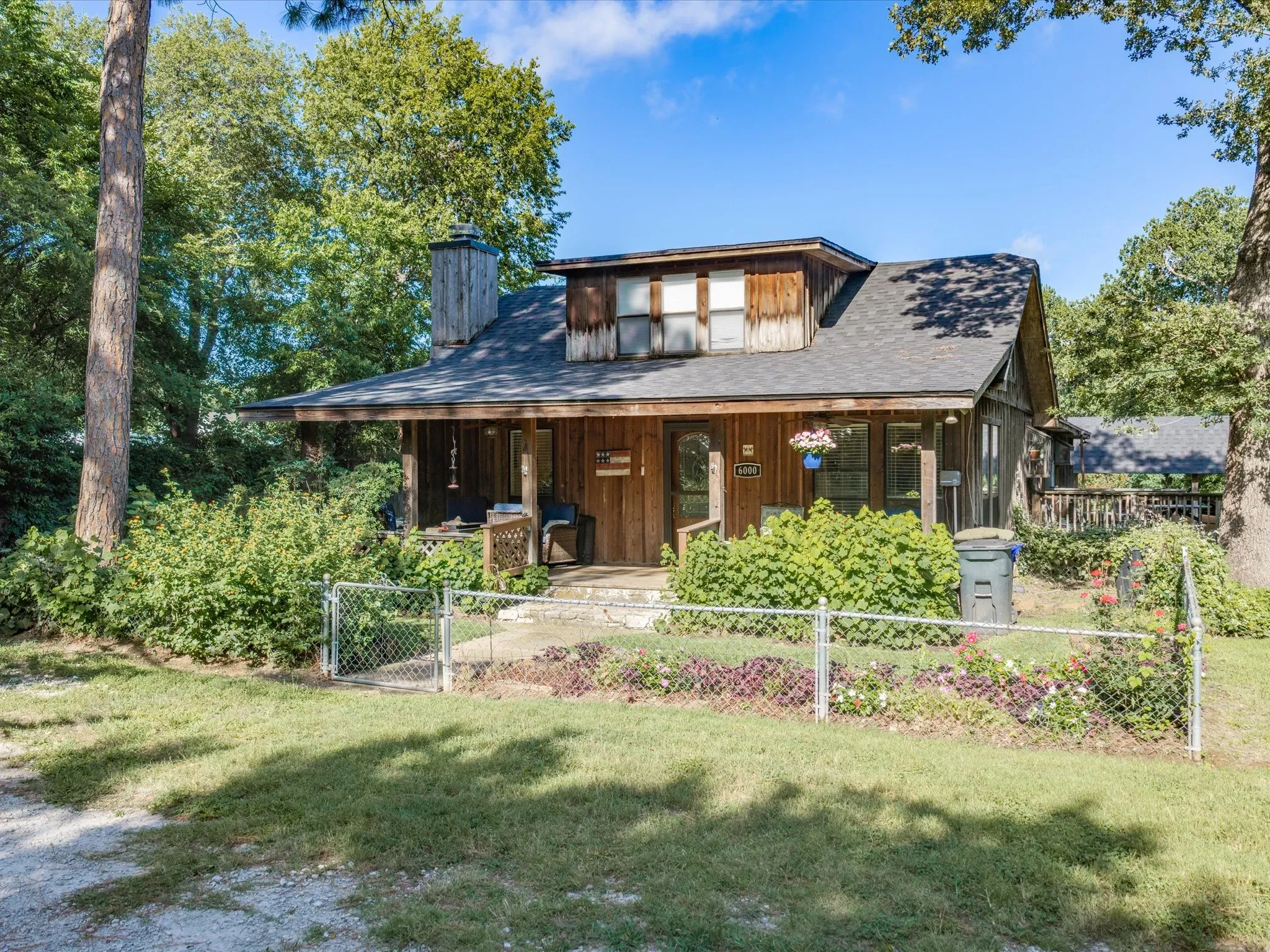 Wood-sided home featuring a covered front porch, dormer window, and chain-link fencing