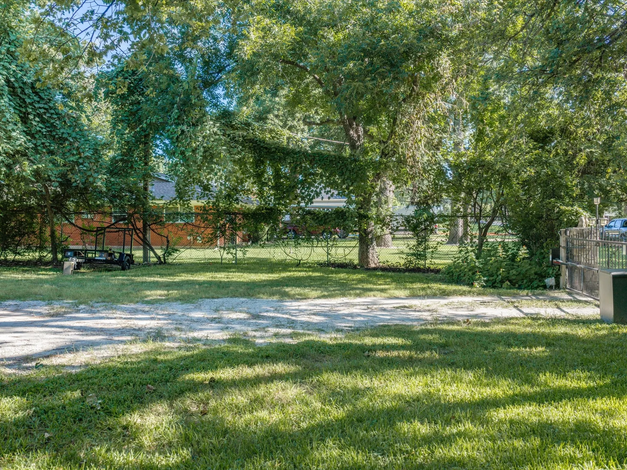 Expansive green lawn with mature trees and a gravel driveway