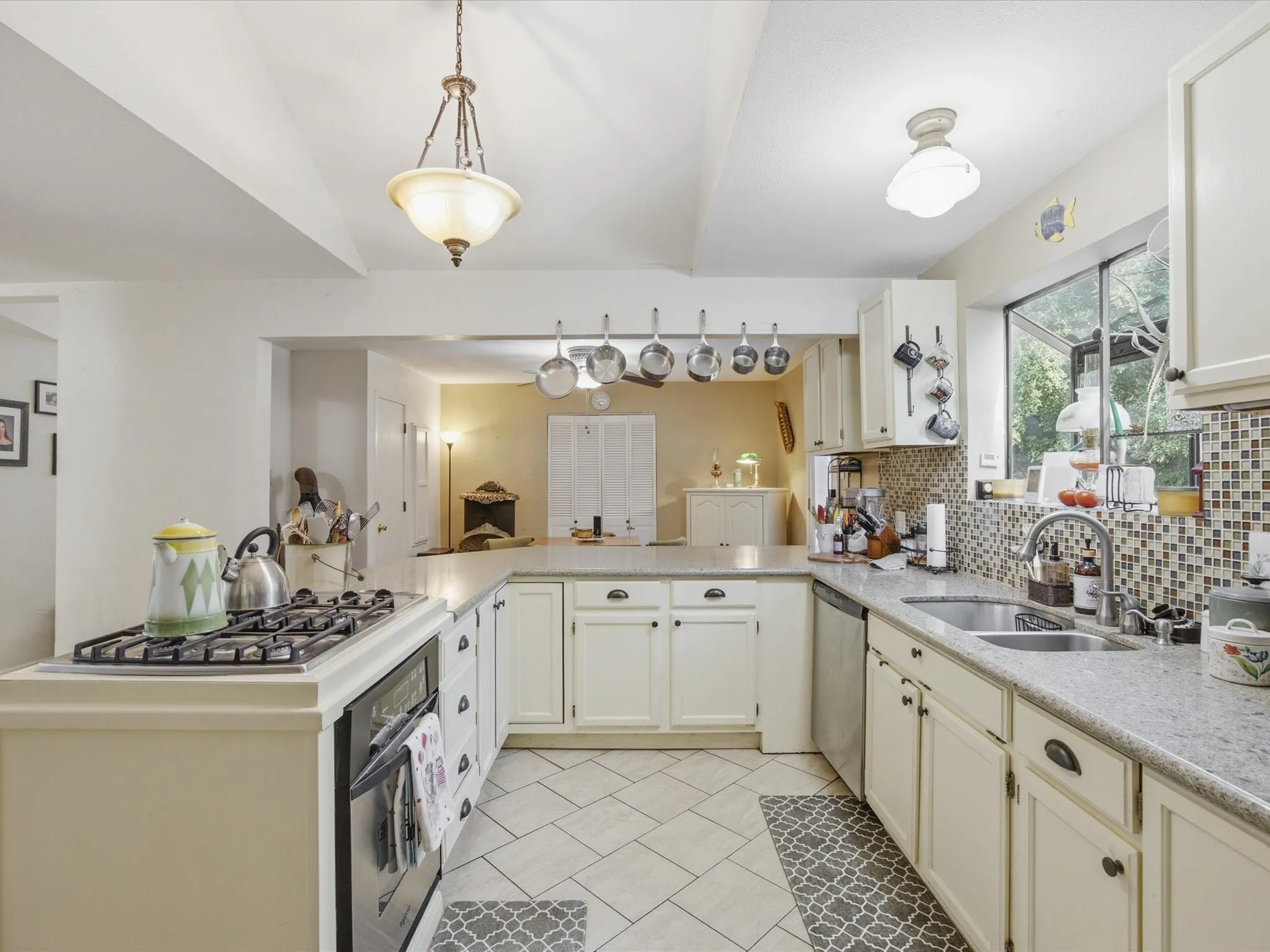 Kitchen featuring a built-in gas range, dual basin sink, white cabinetry with dark hardware, a tiled backsplash, and recessed and pendant lighting