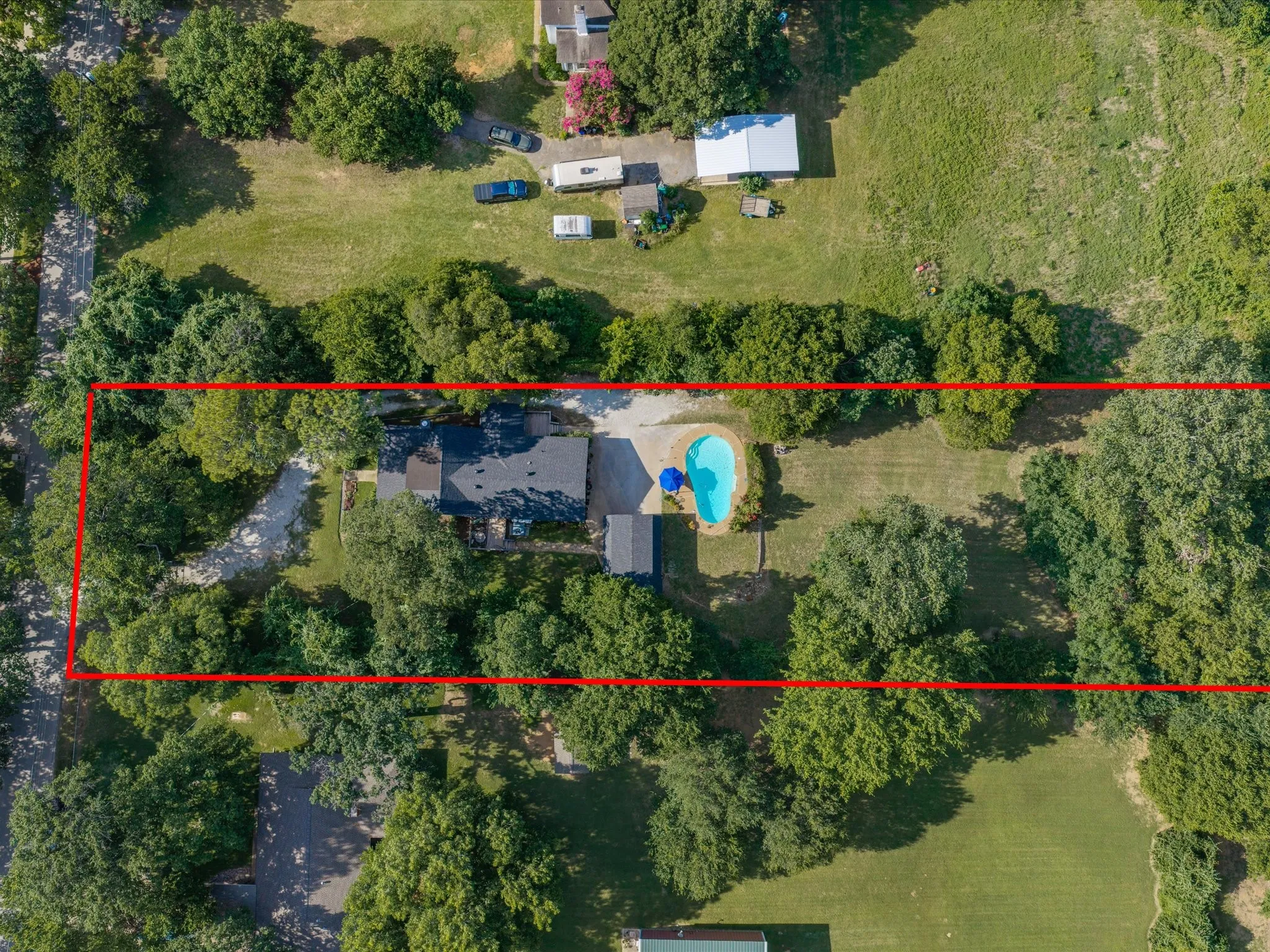 Property featuring a dark-pitched roof, an in-ground swimming pool with a surrounding patio, a concrete driveway, and mature​​‌​​​​‌​​‌‌​‌‌​​​‌‌​‌​‌​‌​​​‌​​ landscaping