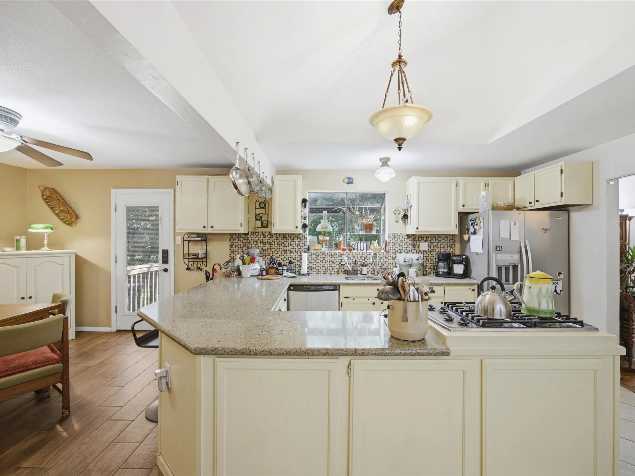 Kitchen featuring a central island with a gas cooktop, cream-colored cabinetry, a mosaic tile backsplash, stainless steel appliances, and wood-finish flooring