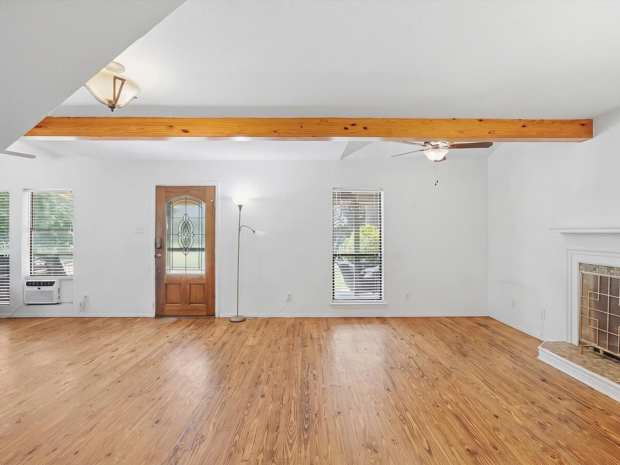 Spacious living area featuring wood-finish flooring, a decorative wooden ceiling beam, and white walls