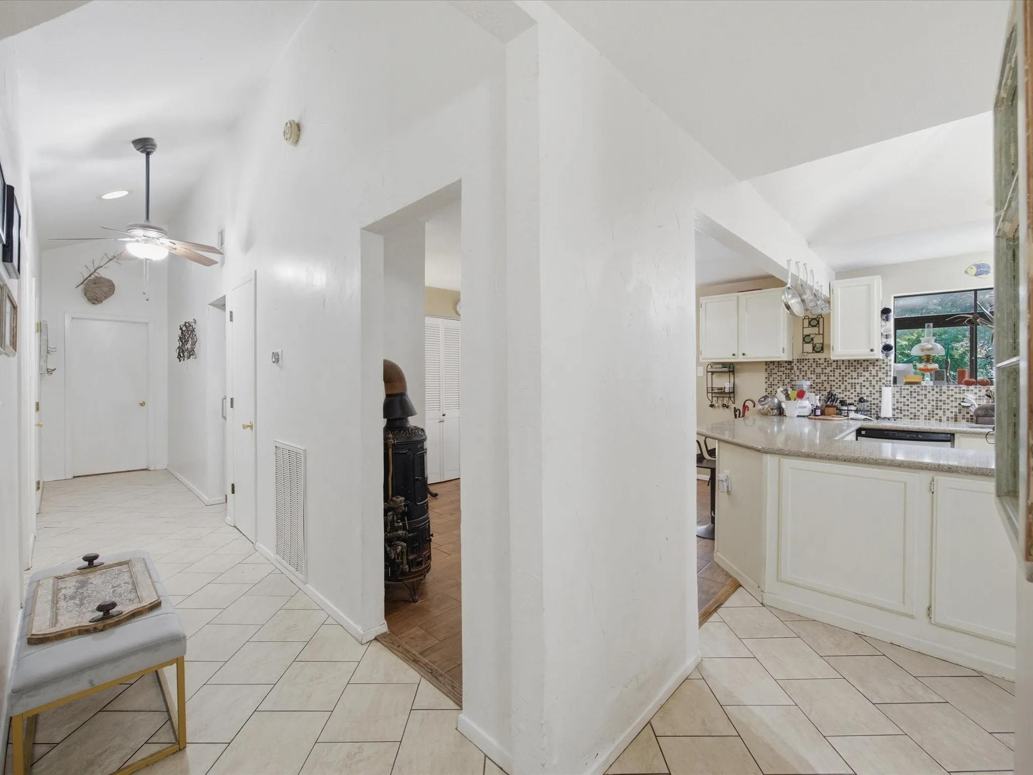 Hallway with diagonal tile flooring leading to a kitchen with light cabinetry, light countertops, and a mosaic tile backsplash
