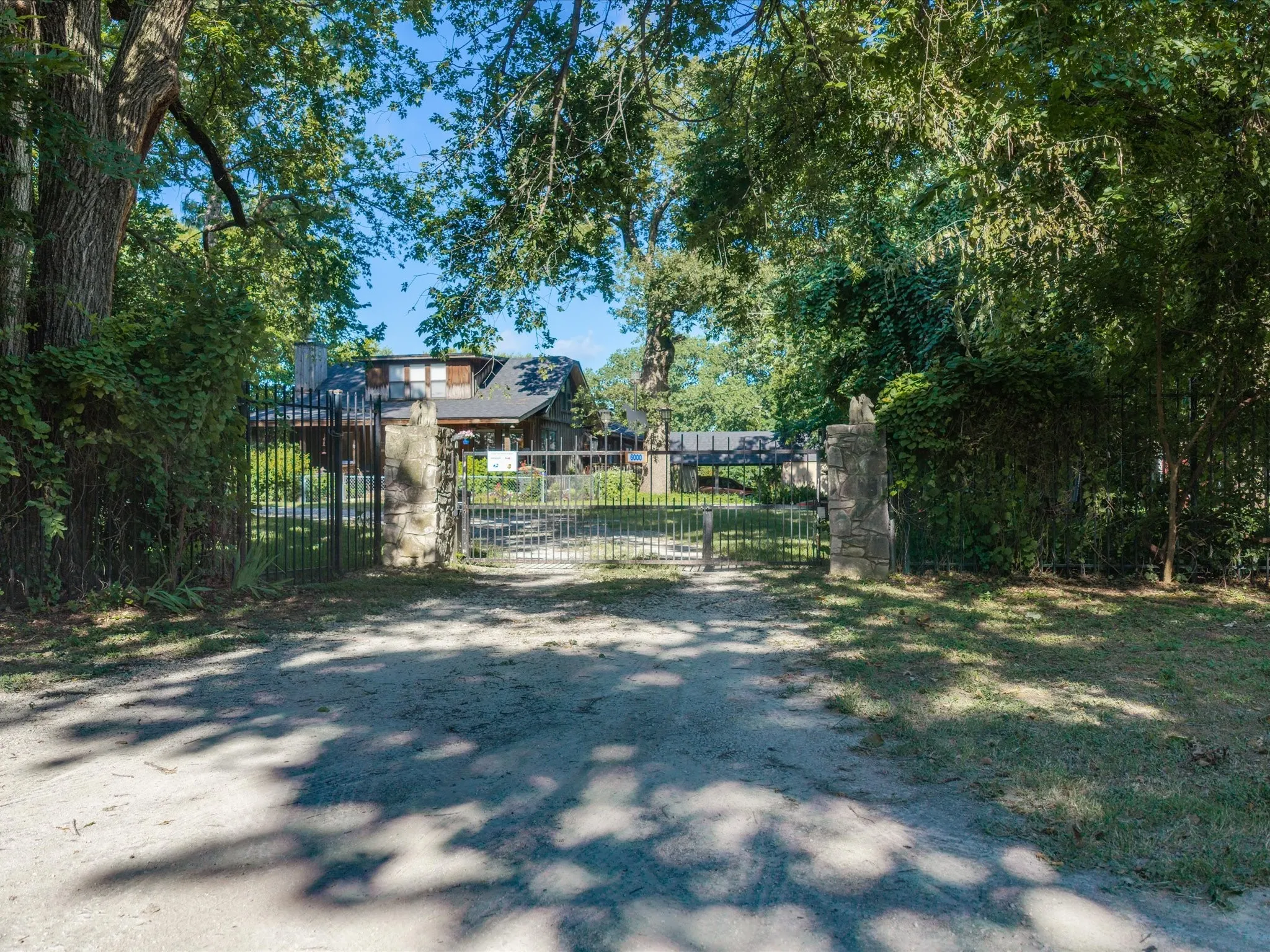 Gated entrance featuring stone pillars and wrought iron fencing, surrounded by mature trees and lush greenery