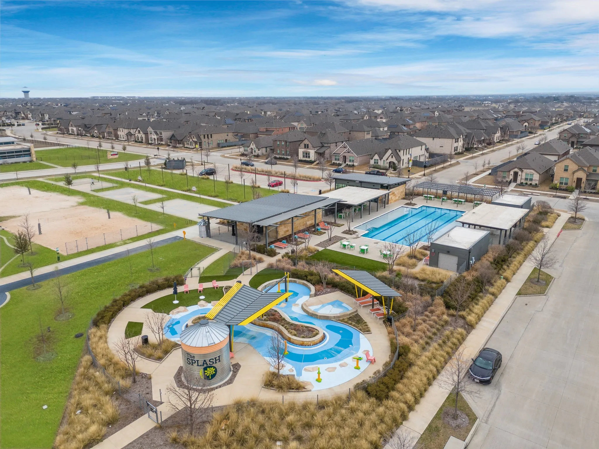 Community amenities featuring a resort-style swimming pool, splash pad, shaded seating areas, and volleyball courts, surrounded by manicured landscaping and residential properties
