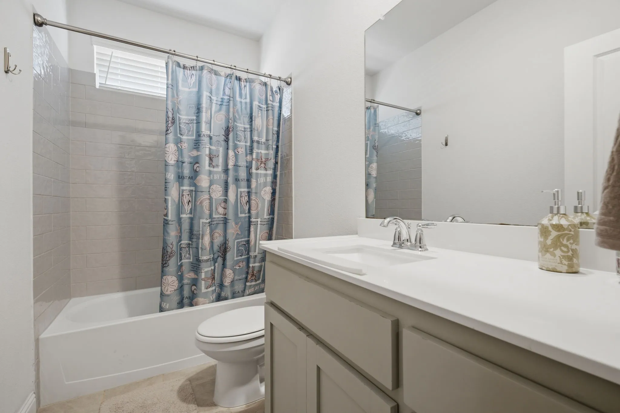 Bathroom featuring a bathtub with tiled surround, a window with blinds, and a vanity with an integrated sink and mirror