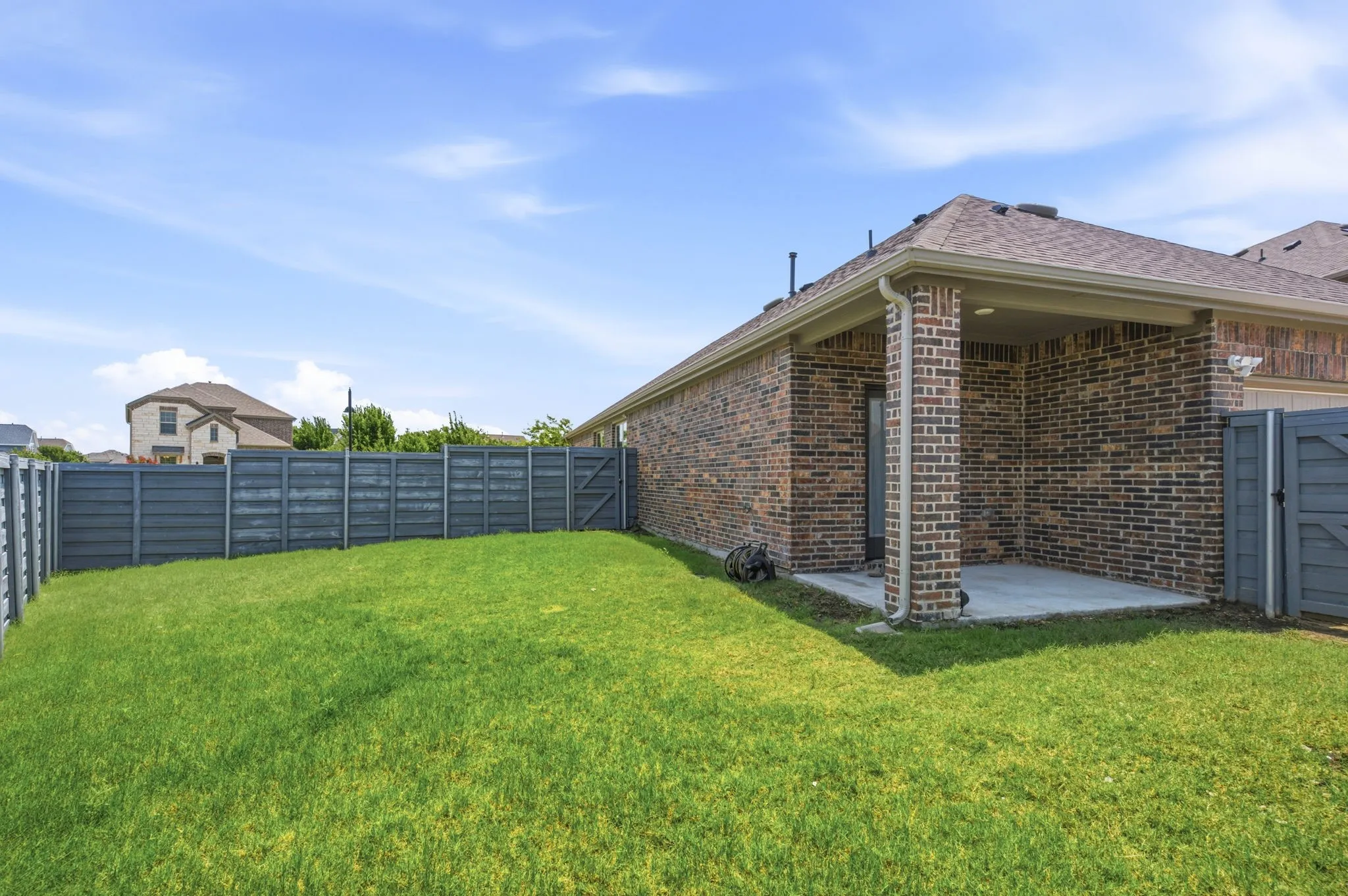 Spacious backyard featuring a covered concrete patio, full privacy fencing, and a brick exterior with gutters