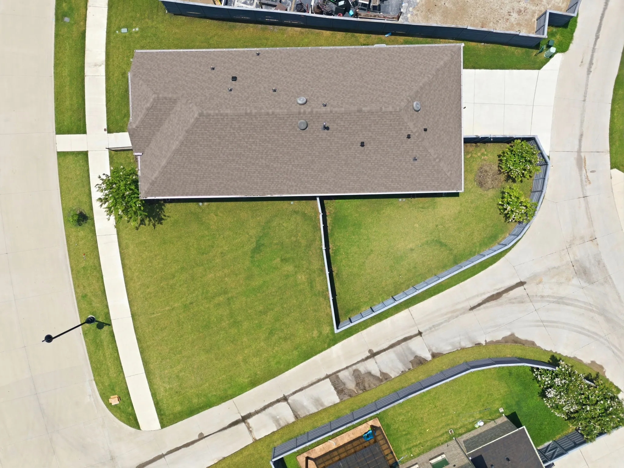 Overhead perspective highlighting the property's brown shingle roof, expansive green lawn, concrete driveway, and surrounding concrete sidewalks