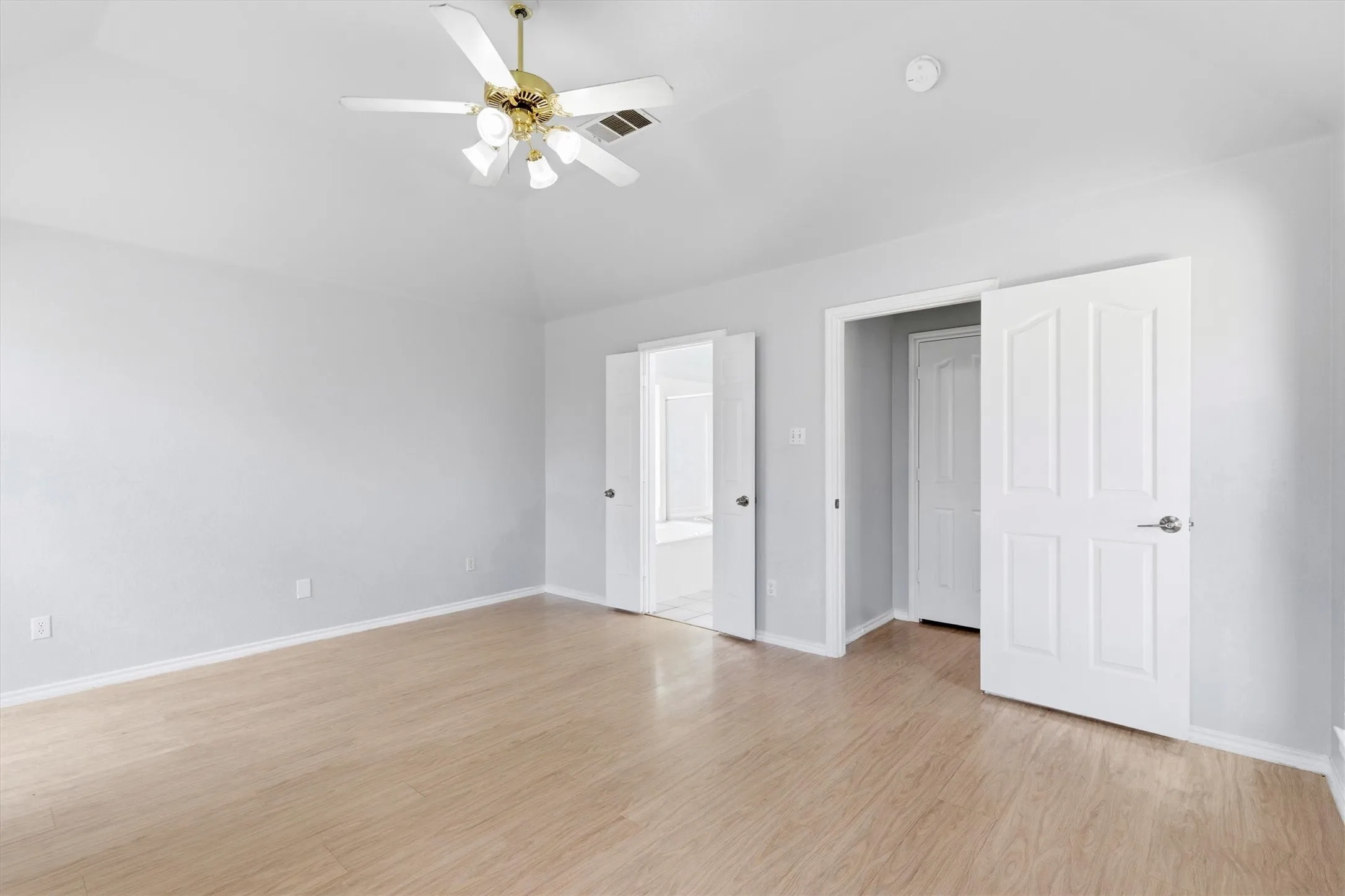 Spacious room featuring light wood-finish flooring, light gray wall tones, and white trim
