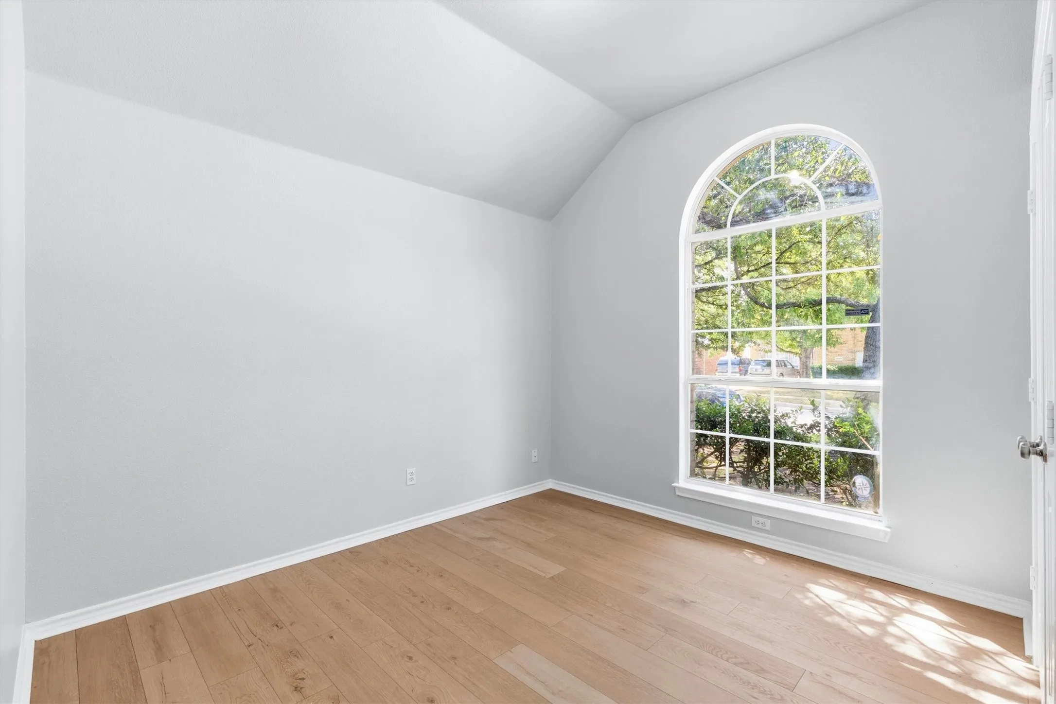 Room featuring a large arched window, wood-finish flooring, white baseboards, and neutral wall paint
